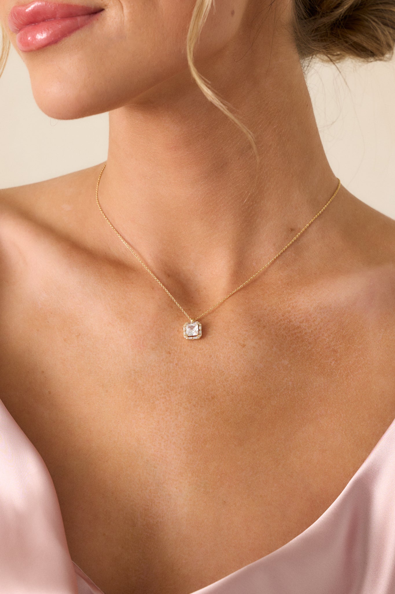 Focused view of the gold necklace, highlighting the delicate thin chain and the square pendant with a large rhinestone centerpiece.