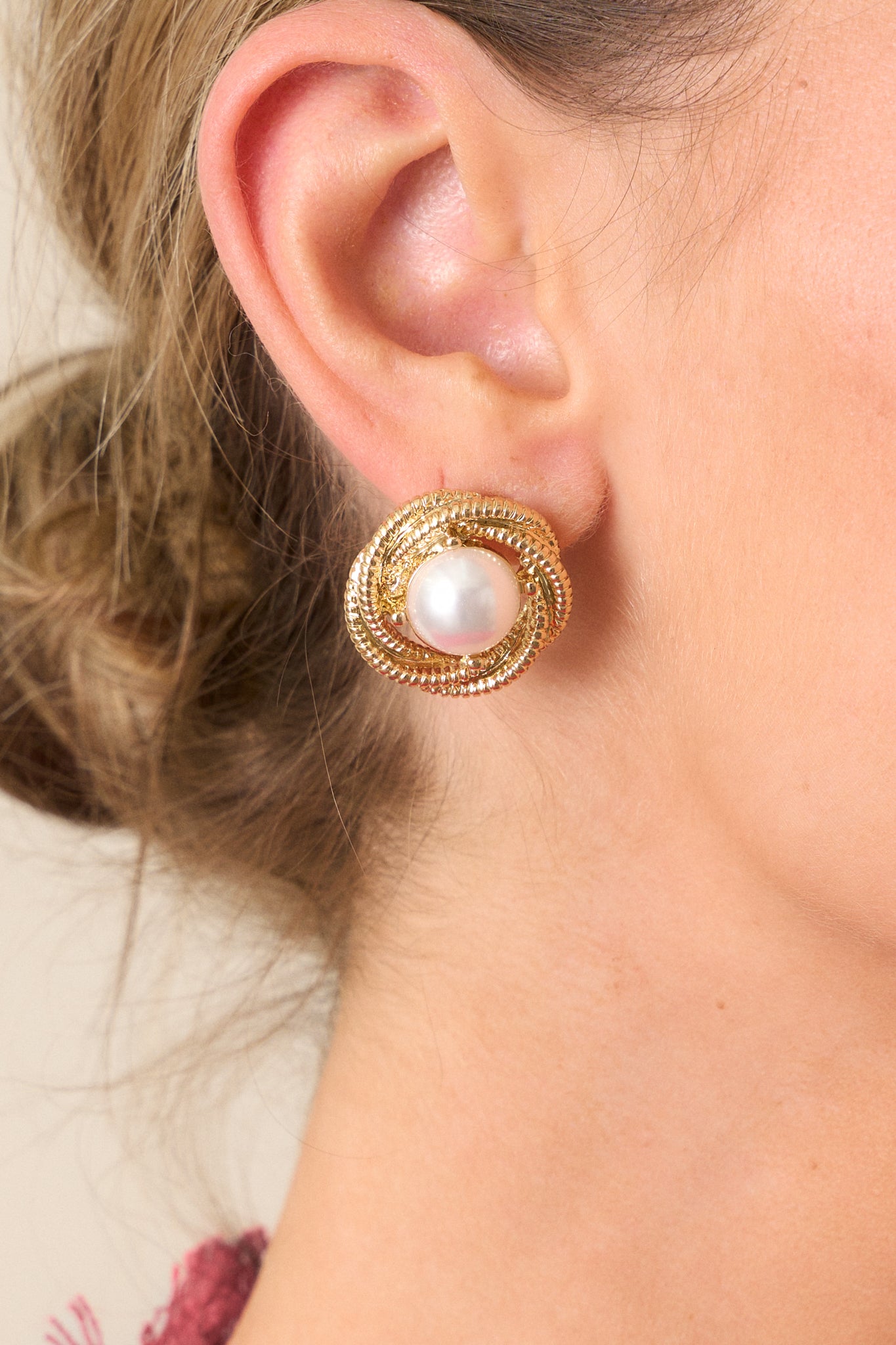 Close up view of these gold earrings featuring gold hardware, a large faux ivory pearl middle, a textured hoop bordering the pearl and secure back postings.&nbsp;