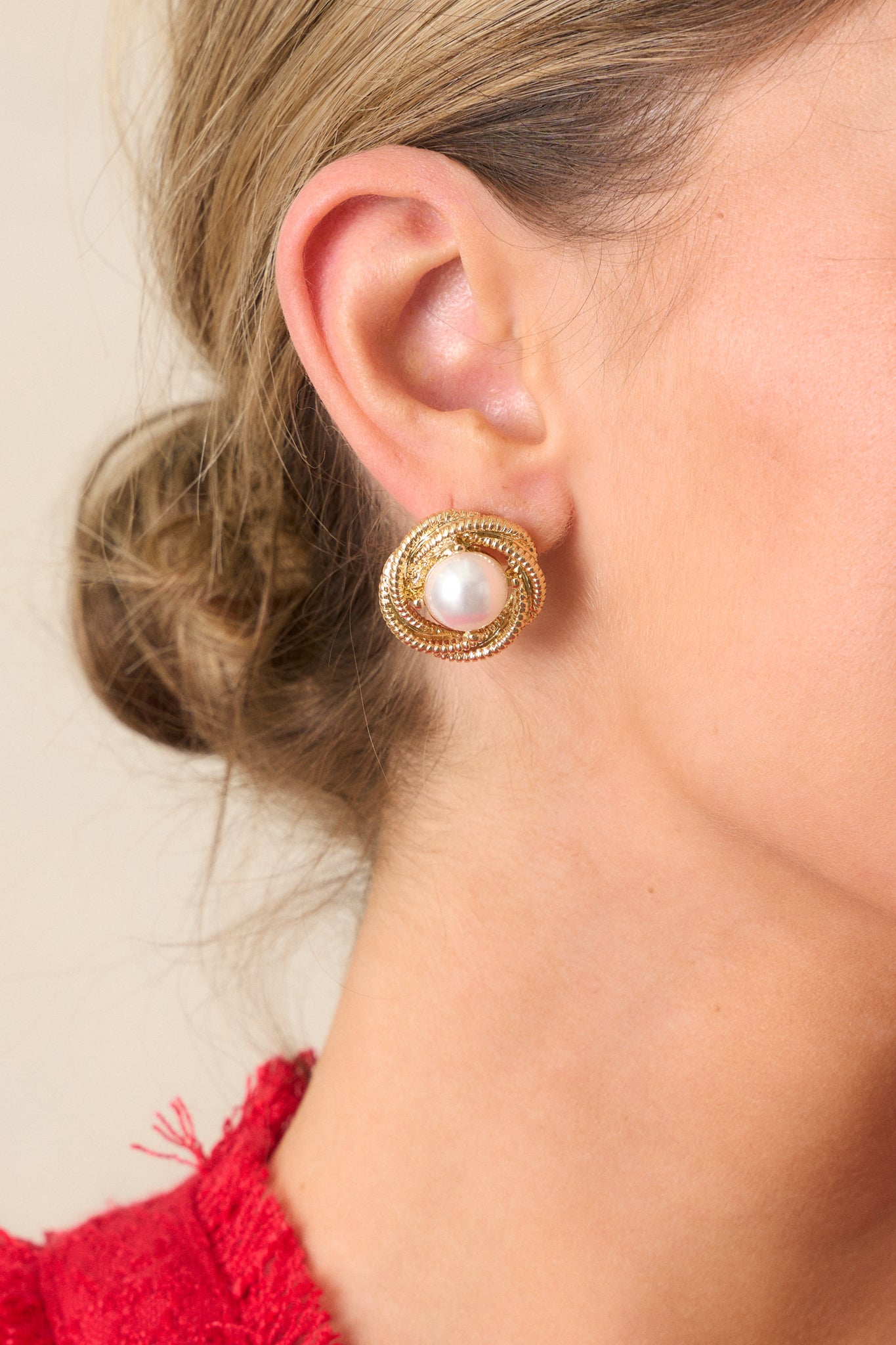 Side view of the gold earring, emphasizing the intricate texture of the hoop and the smooth surface of the faux ivory pearl.