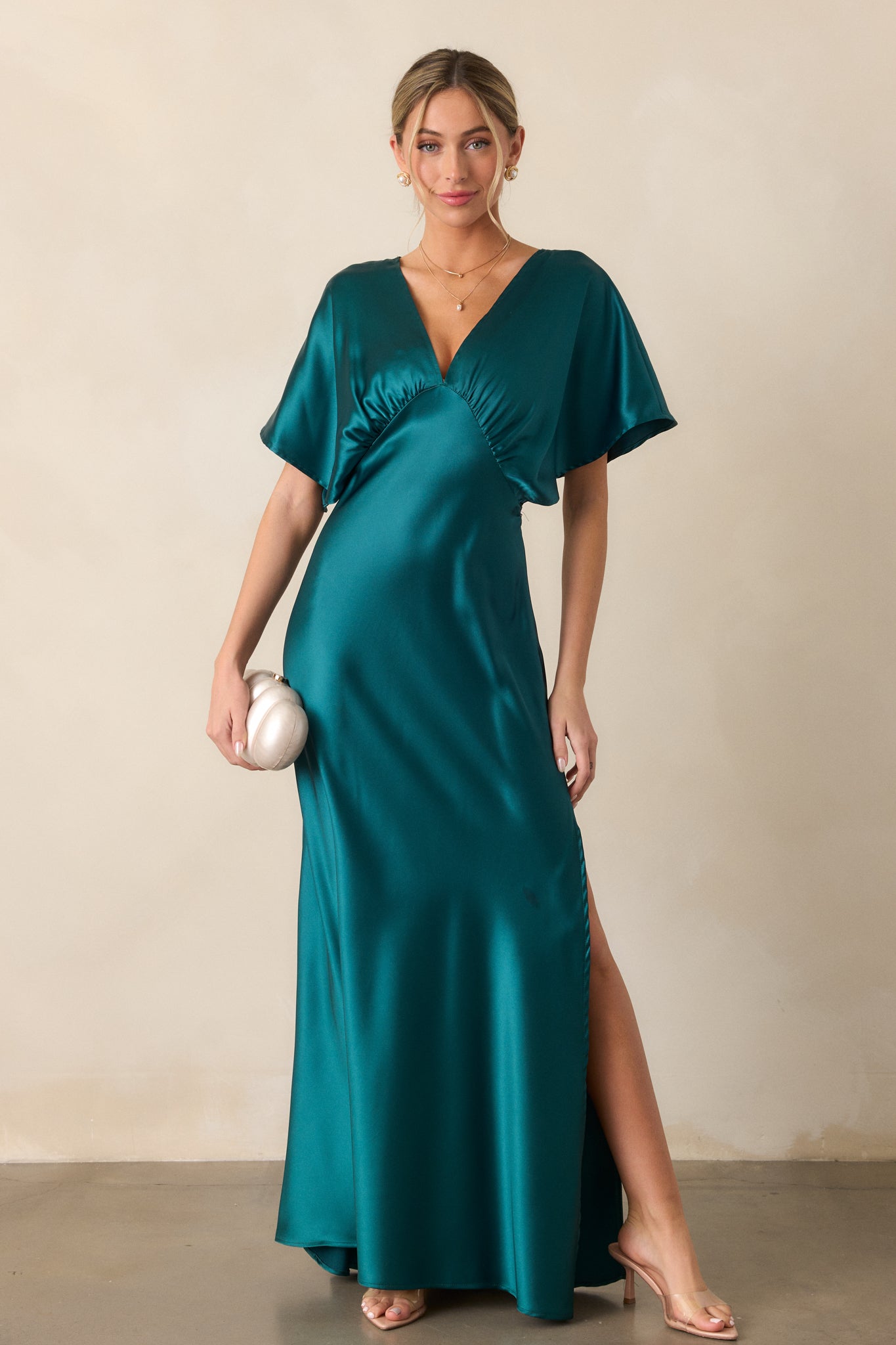 A full-body view of the teal dress featuring a deep V-neckline, kimono-style sleeves, and a side slit. The shiny satin fabric reflects light, adding a luxurious touch.