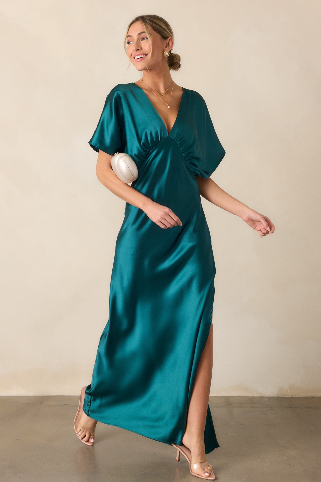 The teal dress with a deep V-neckline and kimono-style sleeves, shown in a relaxed pose. The side slit and satin fabric give it an elegant, flowing silhouette.