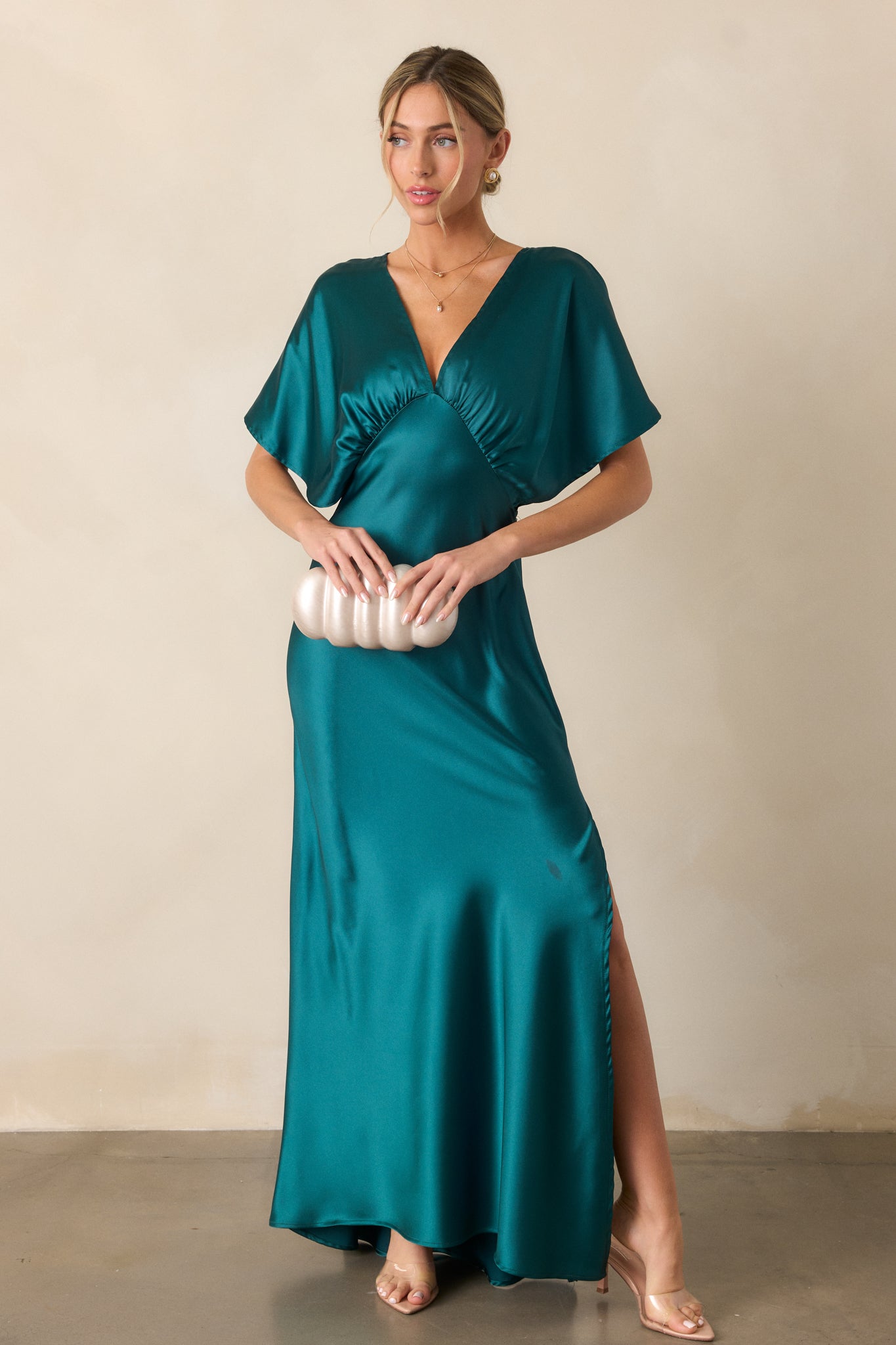 A full-body shot of the teal satin dress with kimono-style sleeves and a deep V-neckline. The side slit adds movement to the dress, highlighting the fabric's shine.