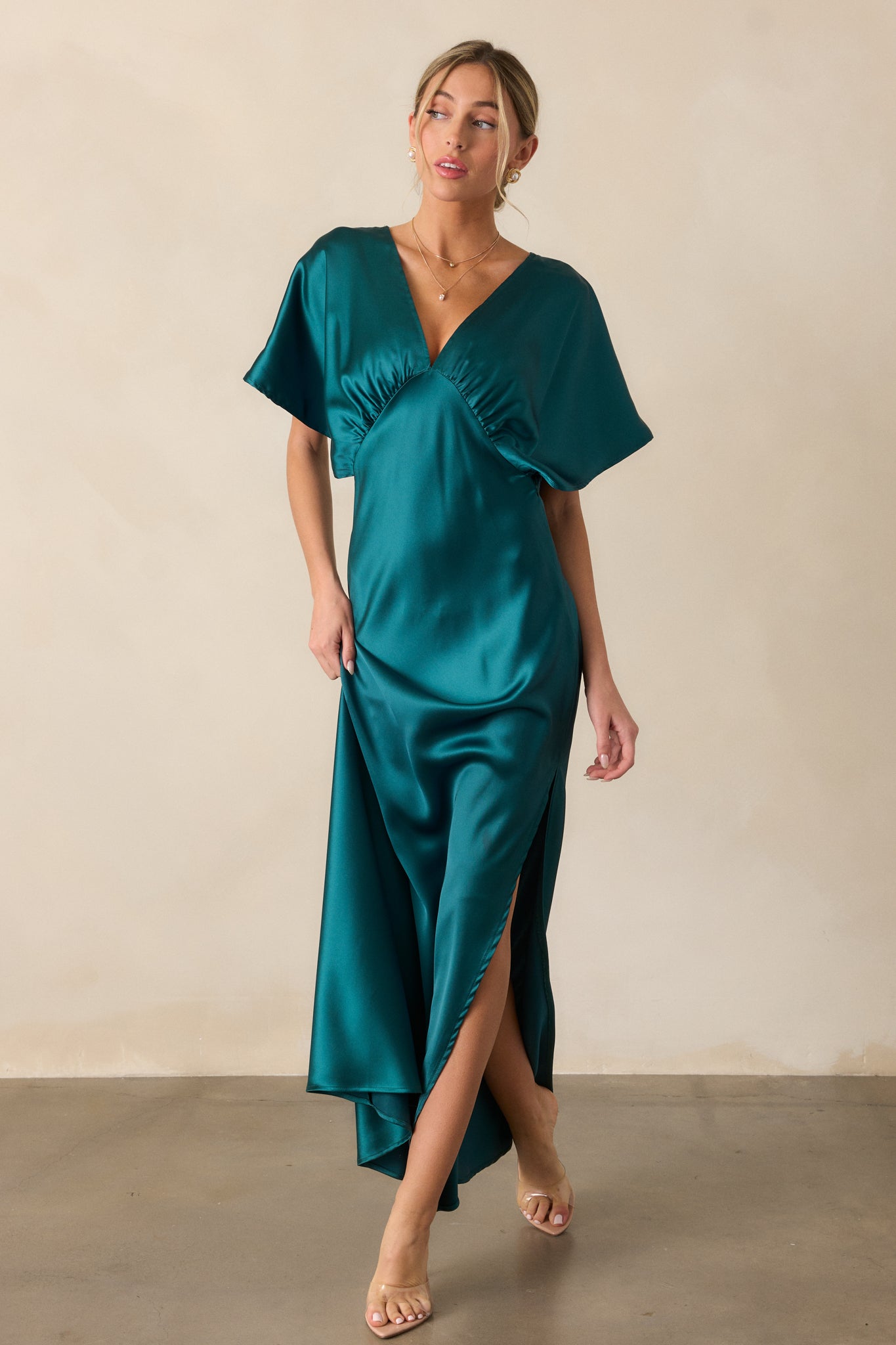 A front view of the teal dress with a deep V-neckline and flowing kimono sleeves, showcasing the soft sheen of the satin fabric and the graceful side slit.