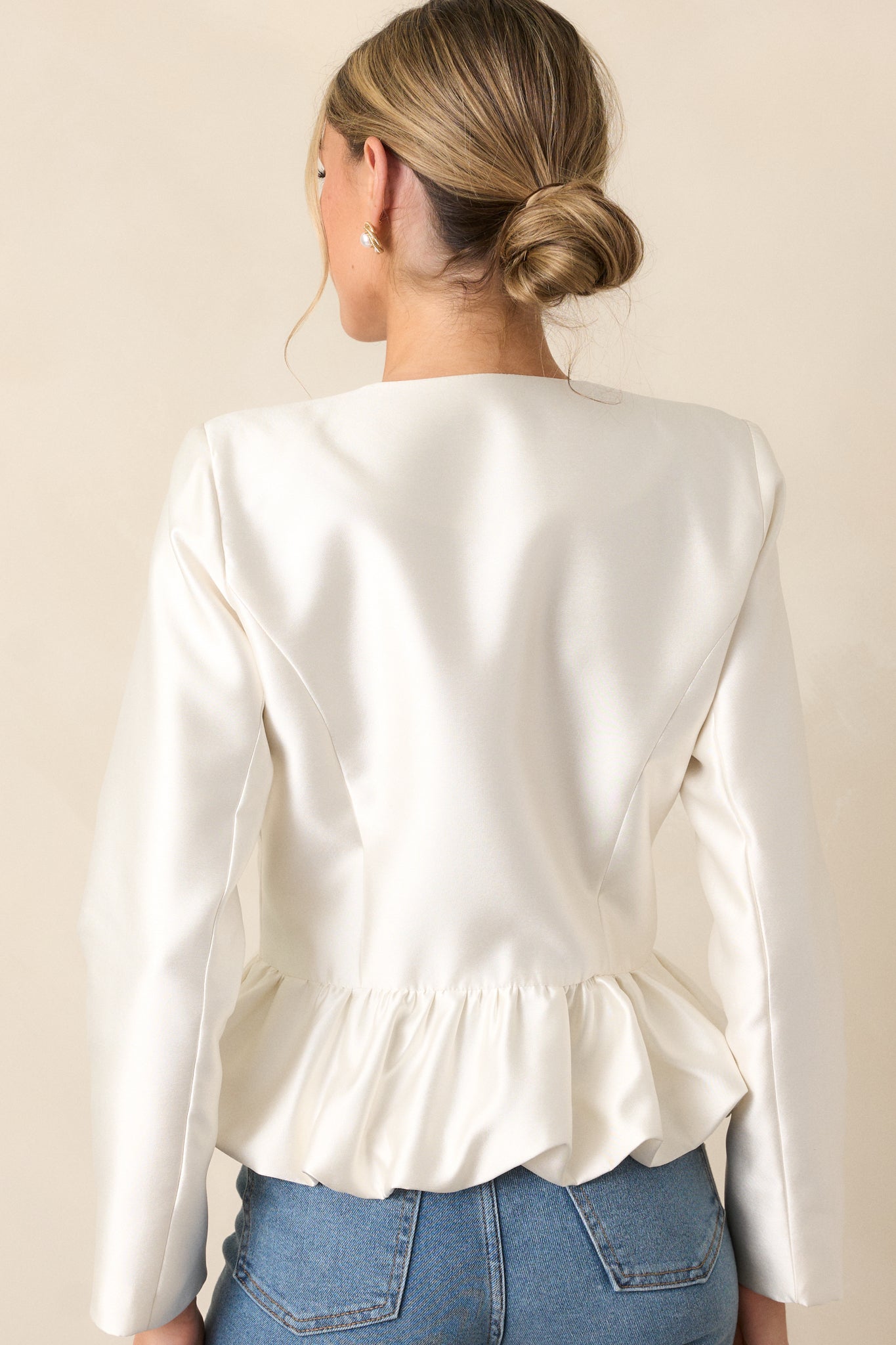 Back view of the ivory top, showing the long sleeves and how the thick satin material drapes over the body, with a focus on the peplum design.