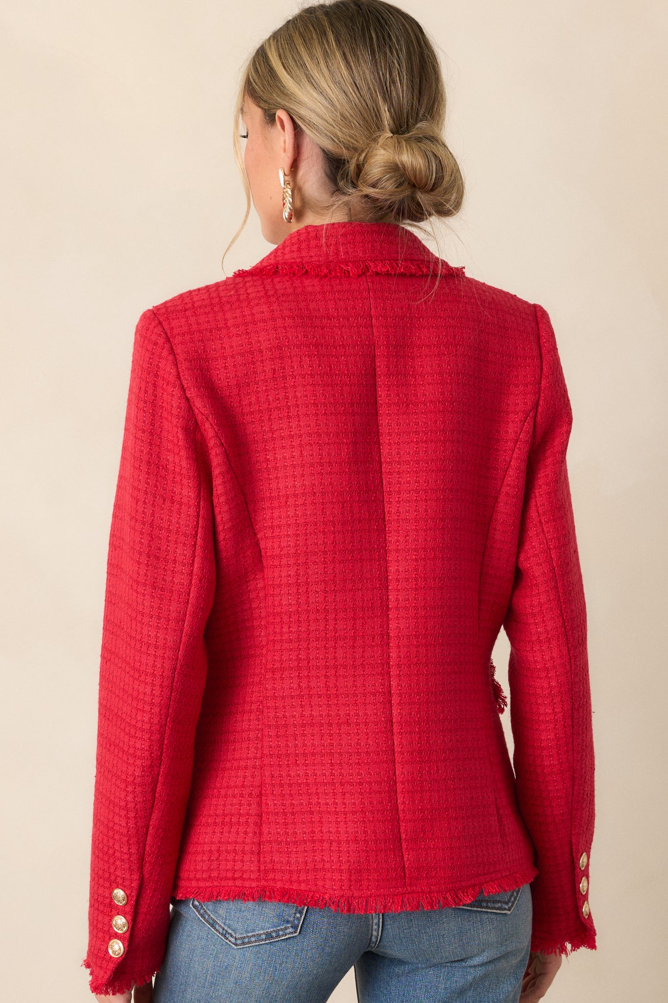 A back view of the red blazer, emphasizing the clean lines, raw fringe hem detailing, and long sleeves.