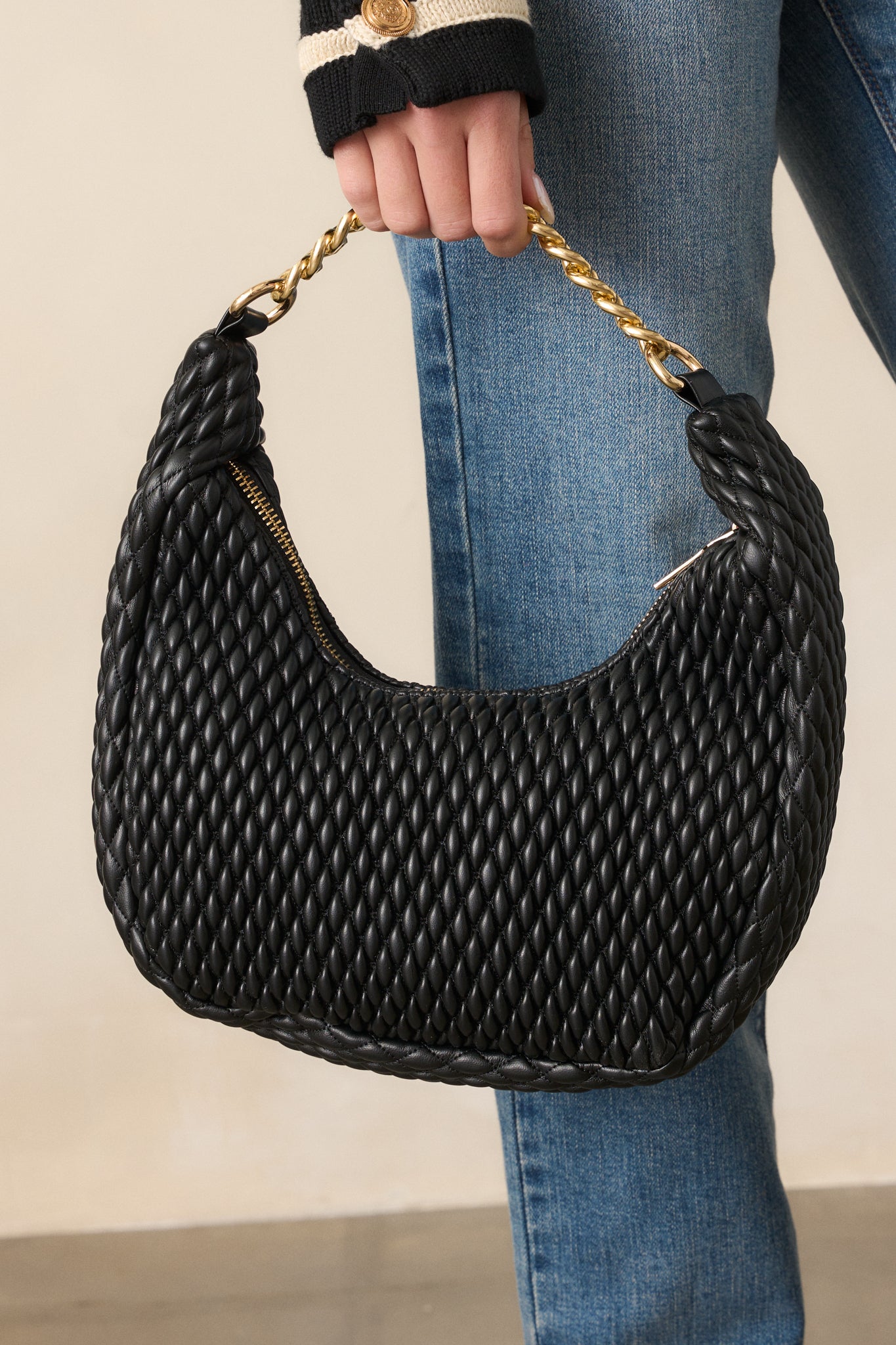 A close-up of the black handbag’s top, focusing on the thick gold chain handle and gold zipper. The faux leather material with a bubbled texture is visible, giving the bag a luxurious appearance.