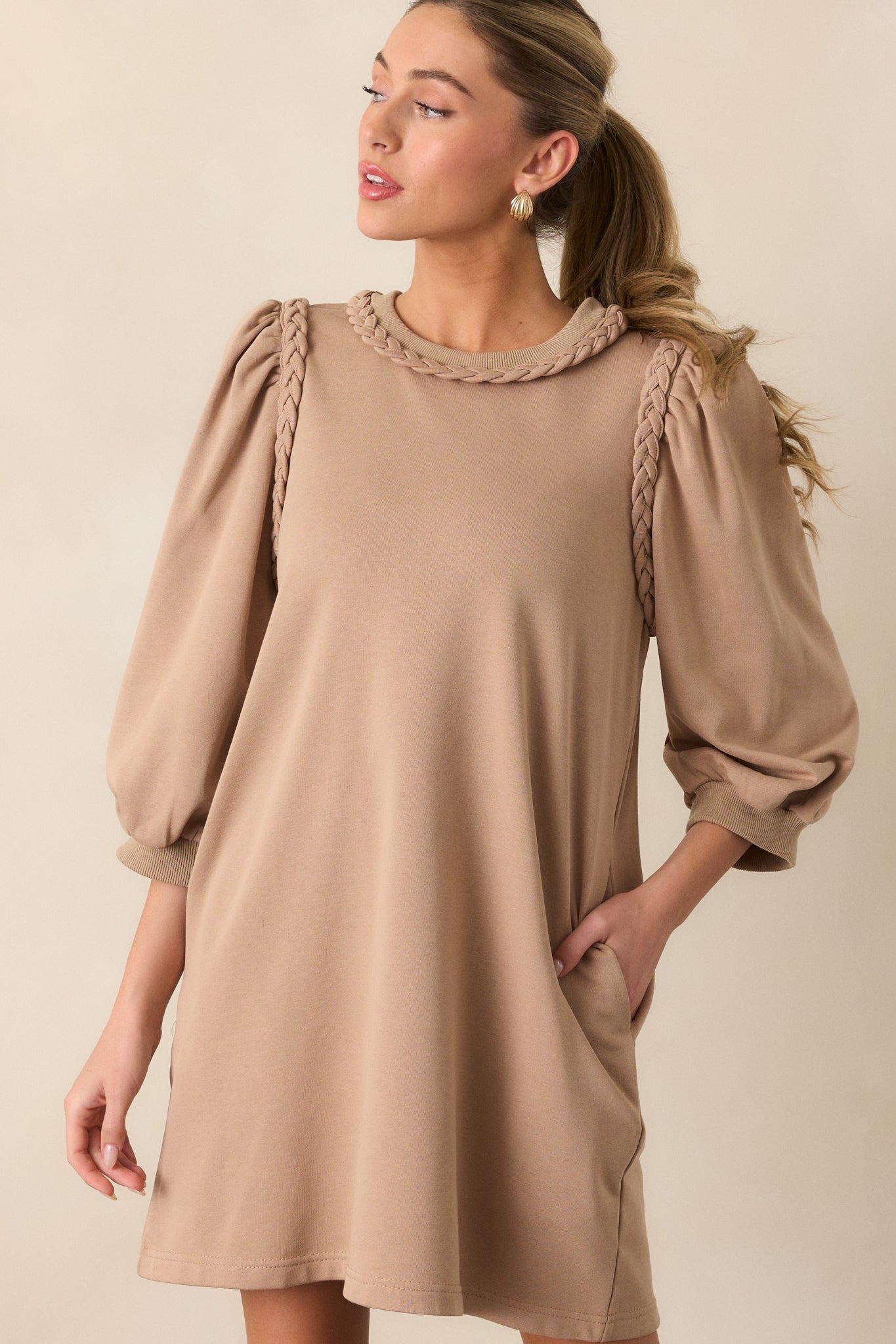 Tan mini dress featuring a braided crew neckline, braided detailing at the shoulders, ribbed cuffs, a box fit, and 3/4 sleeves.