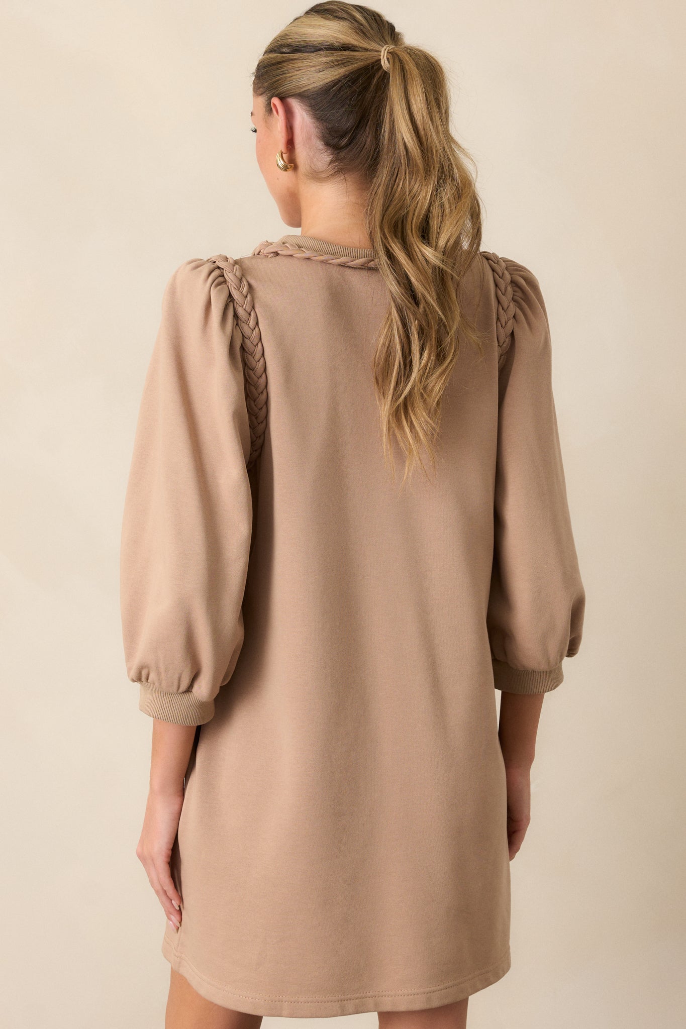 Back view of a tan dress featuring a braided neckline, braided shoulder detailing, puff 3/4 sleeves and a boxy fit.