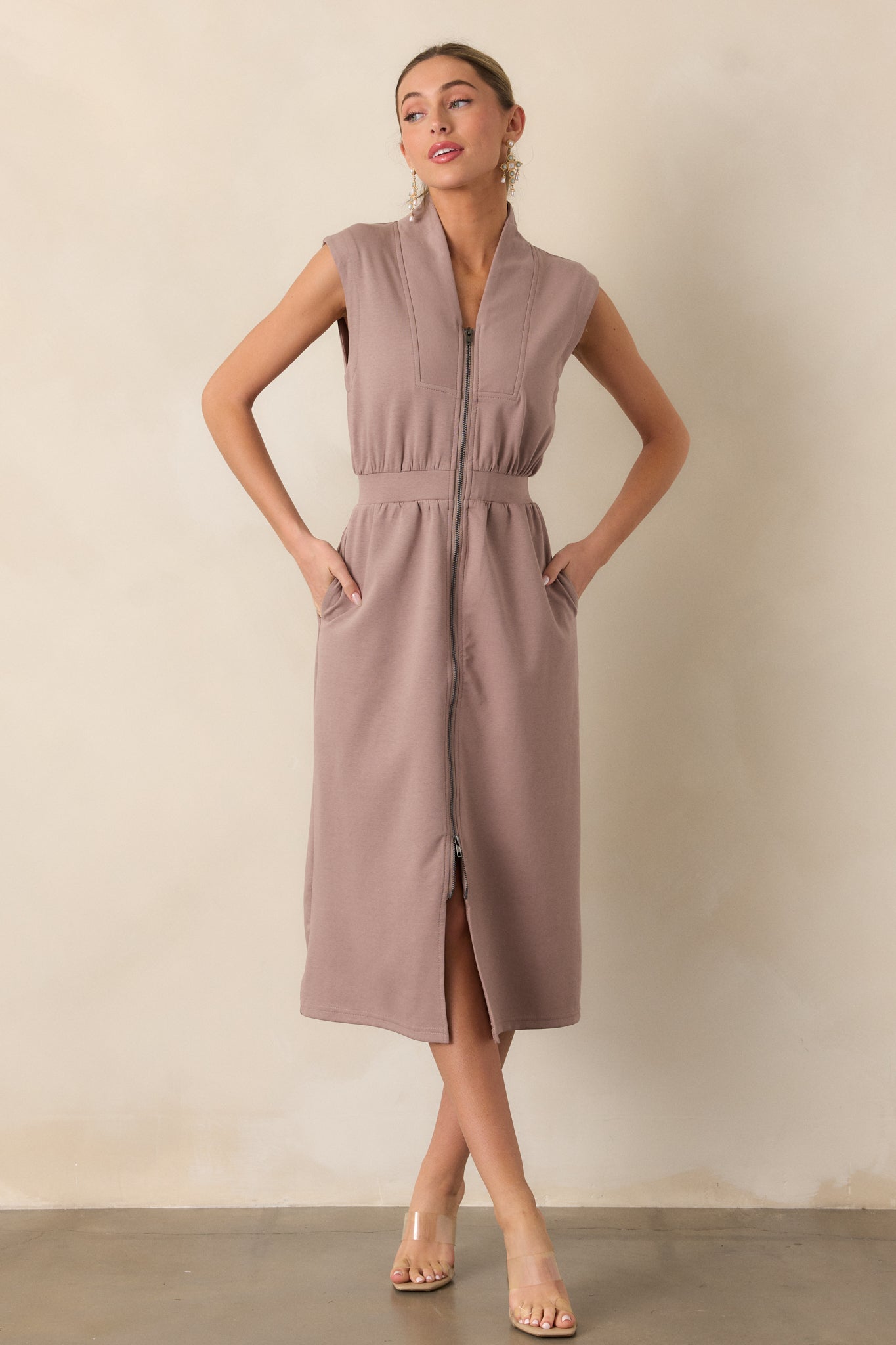 A full-length shot of a dress with a defined, cinched waist thanks to an elastic waistband. The skirt flows softly, creating a smooth, flattering shape, and the dress features functional pockets at the sides for added convenience.