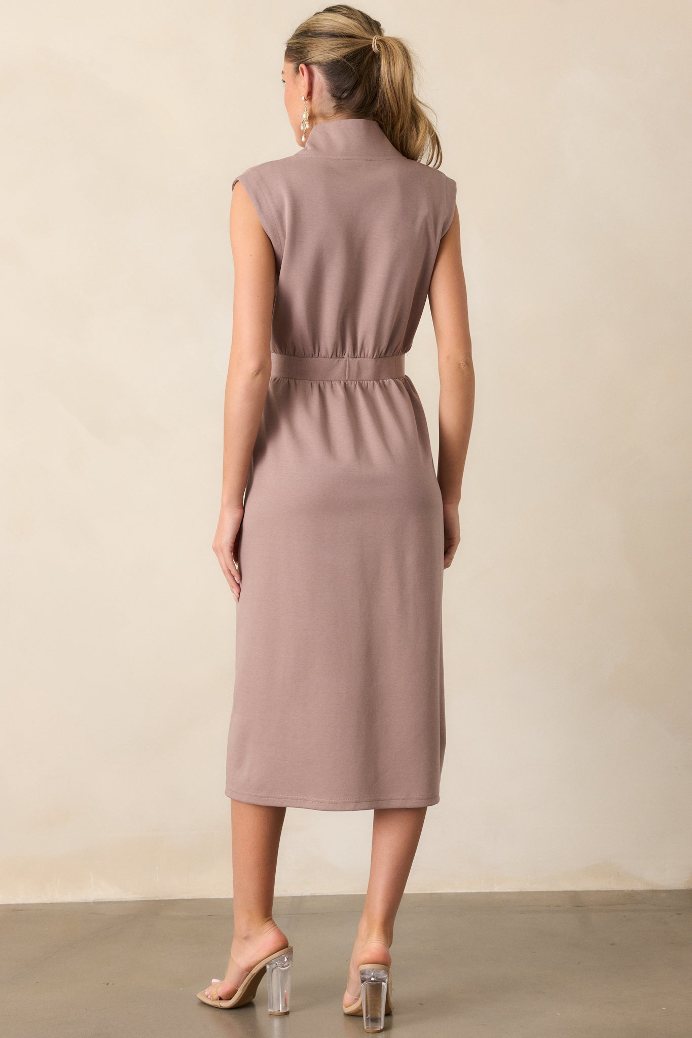 The back view of a taupe dress with a slight collar. The dress features an elastic waistband that cinches the waist, creating a flattering silhouette, while the fabric flows gently down from the waist.