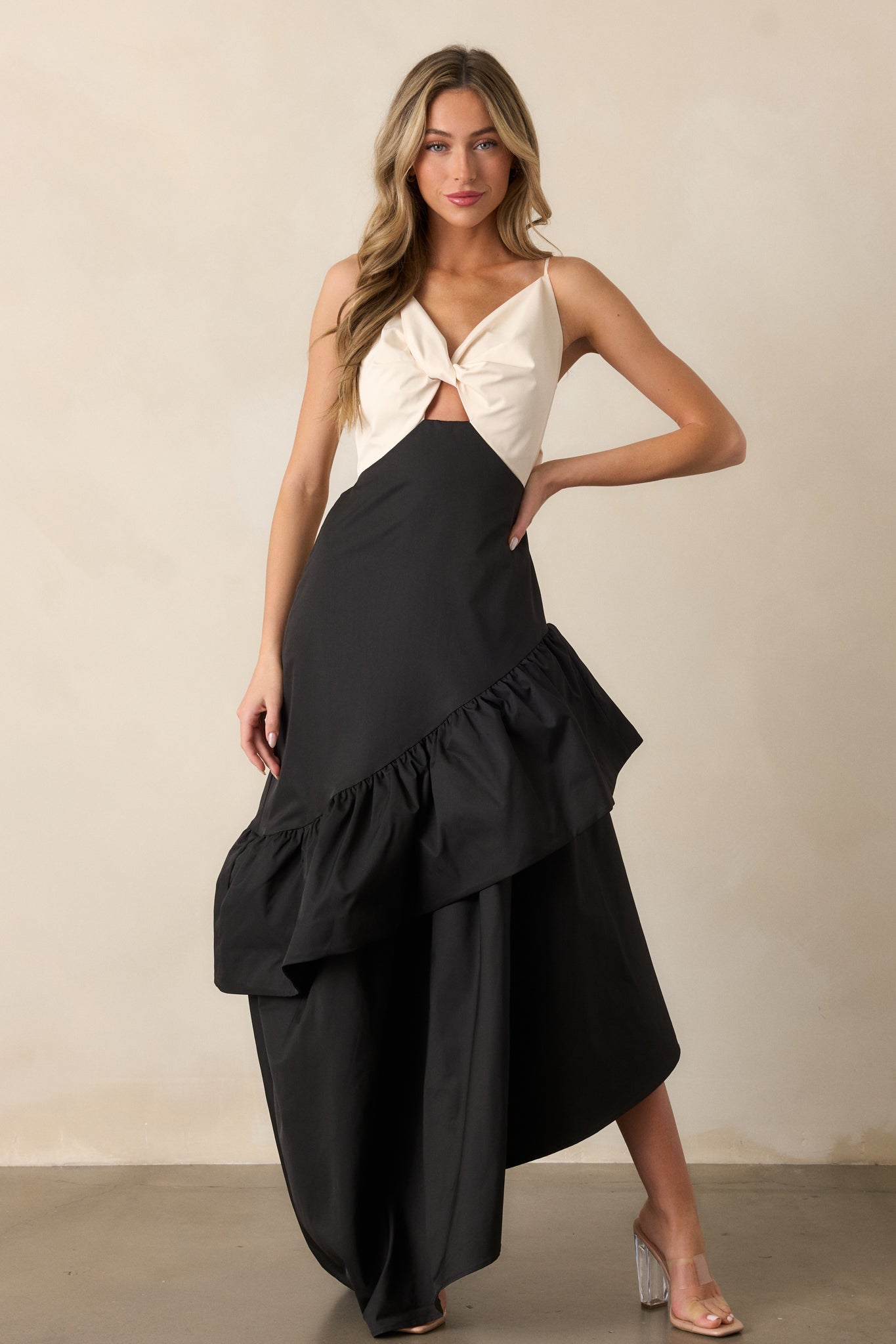 Front-facing view of the black dress showcasing the ivory v-neck top with twist detailing, and the flowing black skirt with a drop waist and ruffled asymmetrical hem.