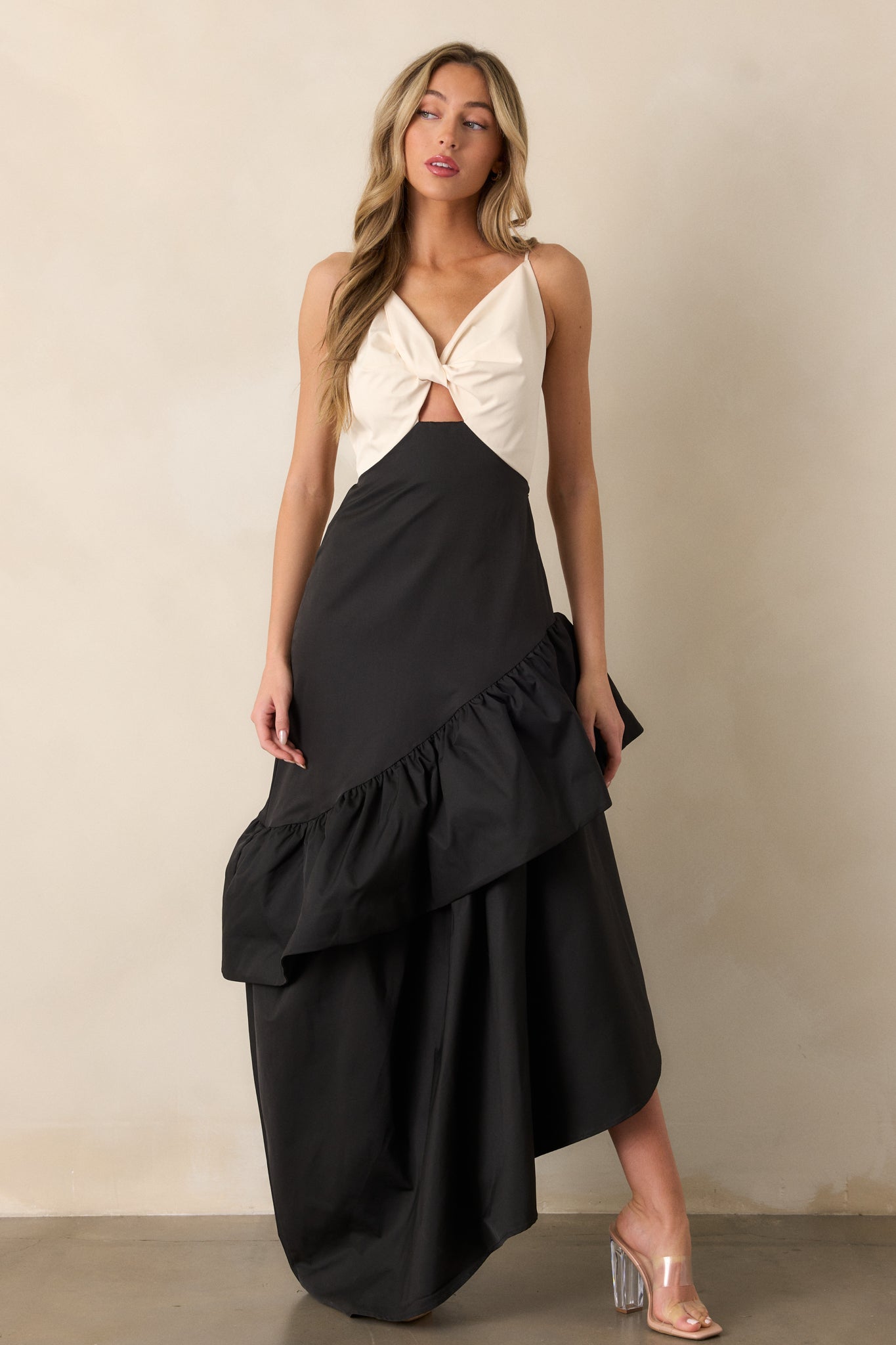 Front view of a black dress with an ivory v-neck top featuring twist detailing, a drop waist design, and an asymmetrical hem with ruffle detailing.