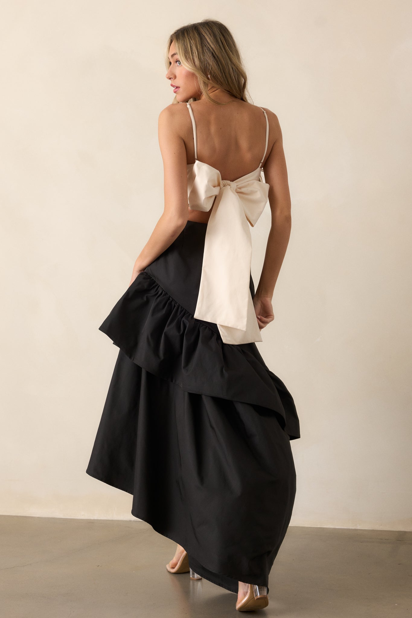 View of the black dress from a slightly turned angle, highlighting the drop waist design and the playful ruffled detailing on the asymmetrical hem