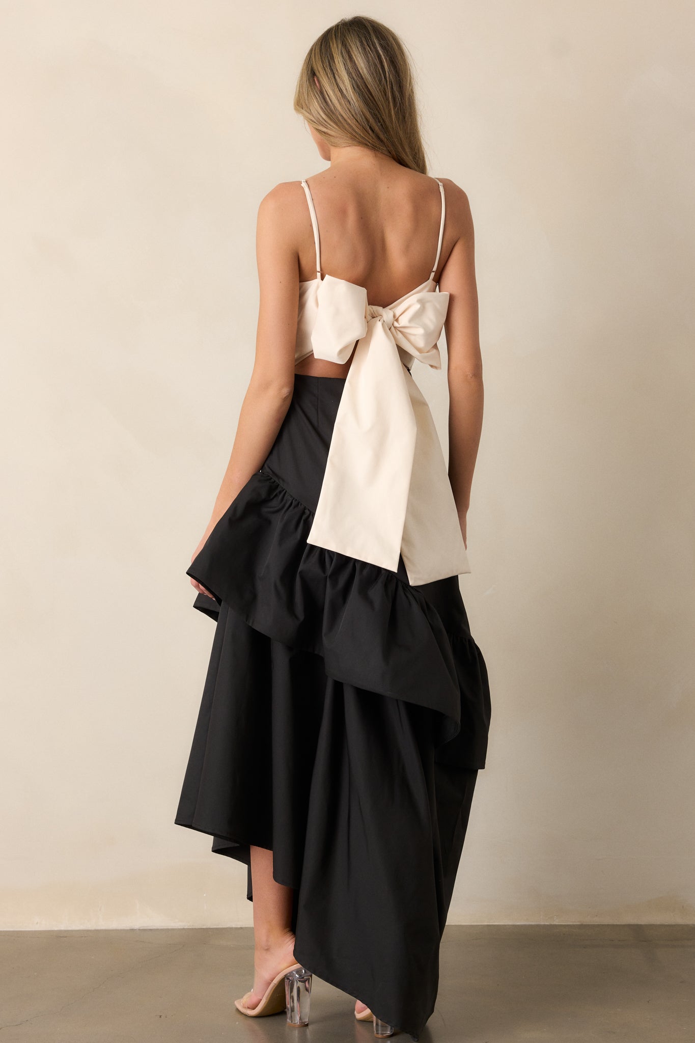 Detailed back view of the black dress, focusing on the self-tie back feature and the discrete back zipper, paired with the flowing ruffled hem.