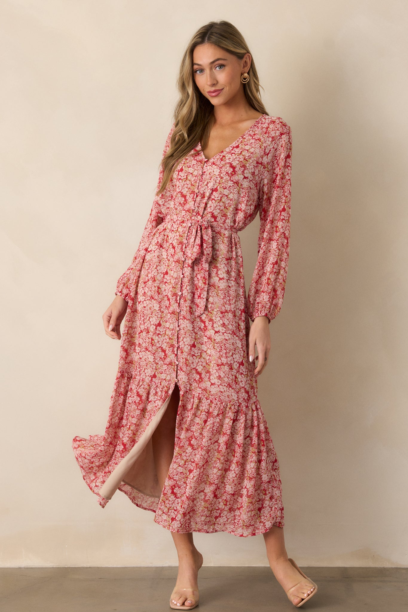 Full view of the cranberry dress featuring a v-neck design, floral print, and long sleeves, with a button front, self-tie waistband, and a tiered midi-length skirt.