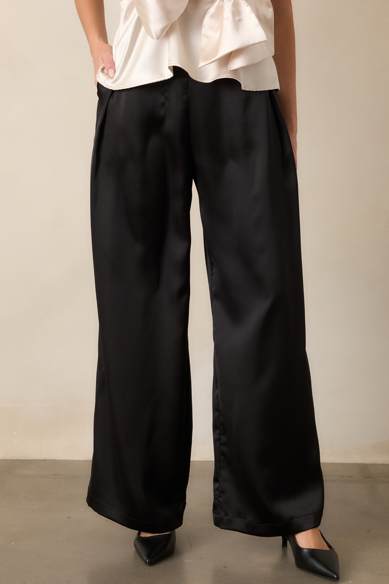 Close-up of the waistband of black satin pants, highlighting the high-waist design and smooth fabric finish.