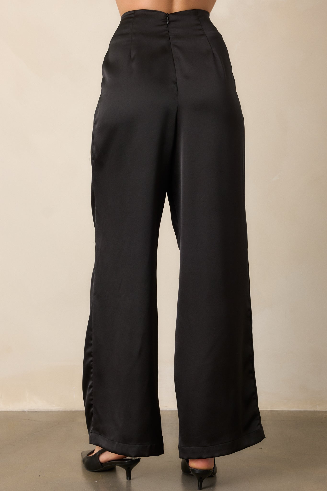 Rear view of high-waisted black pants with a wide leg design, featuring the discrete back zipper and smooth satin texture.