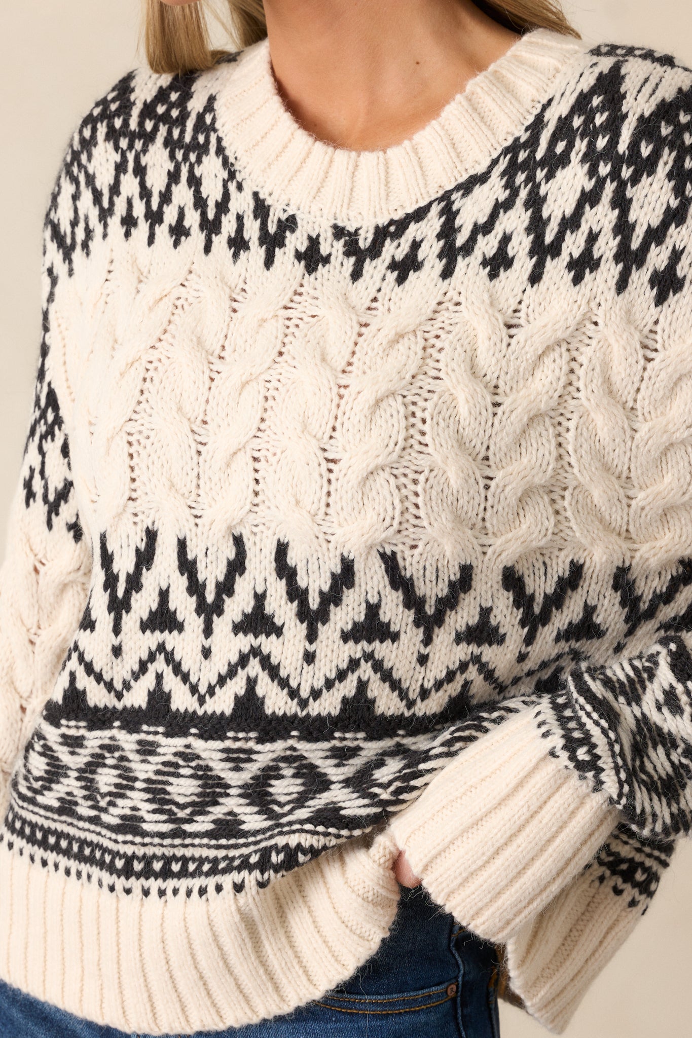 Detailed close-up showing the texture of the cable knit design and the fine ribbing on the neckline of the sweater.