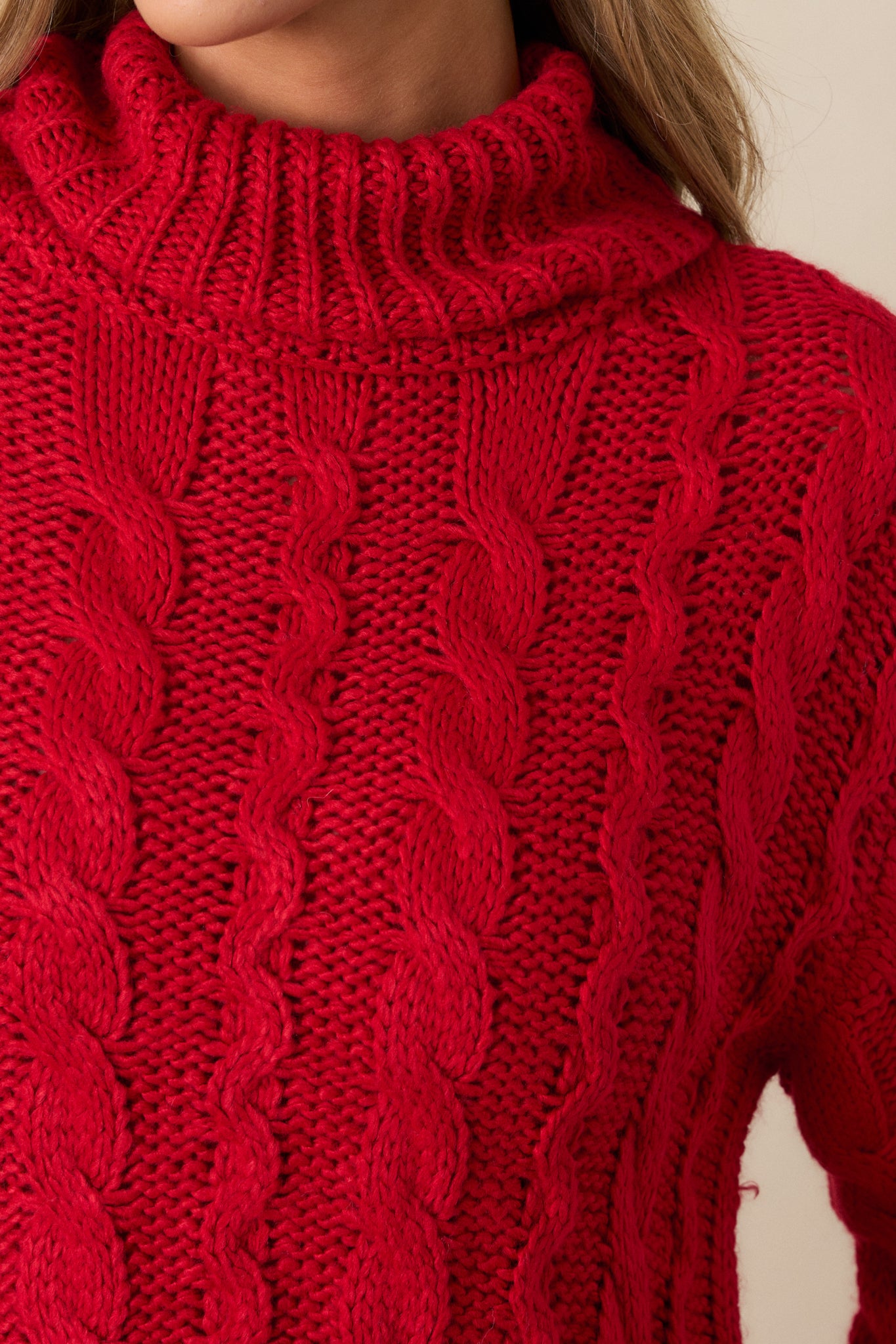 Extreme close-up of the cable knit design on the red sweater, highlighting the texture and craftsmanship of the knit.