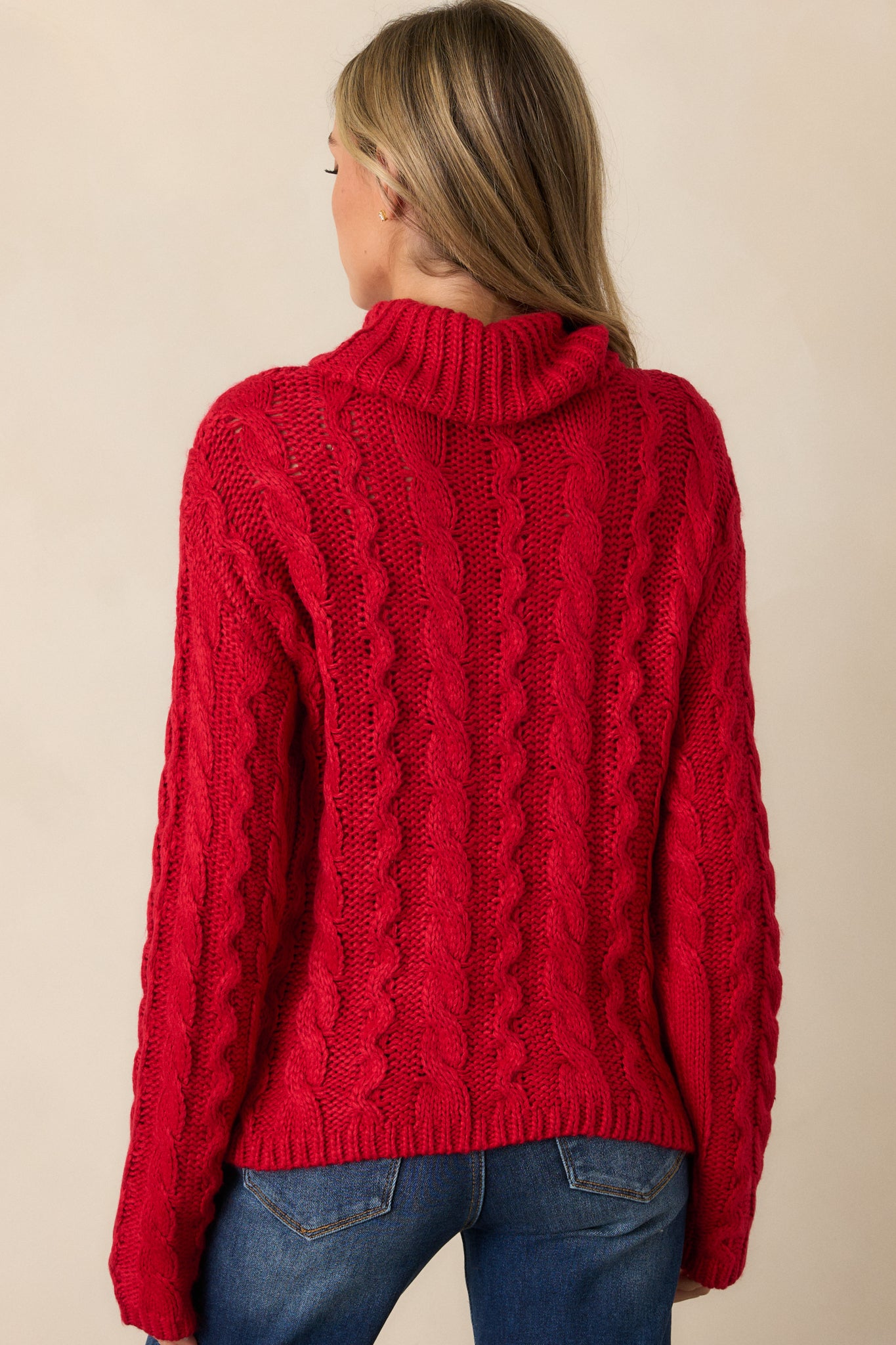 Back view of the red sweater, emphasizing the relaxed fit, long sleeves, and the intricate cable knit design running down the back.