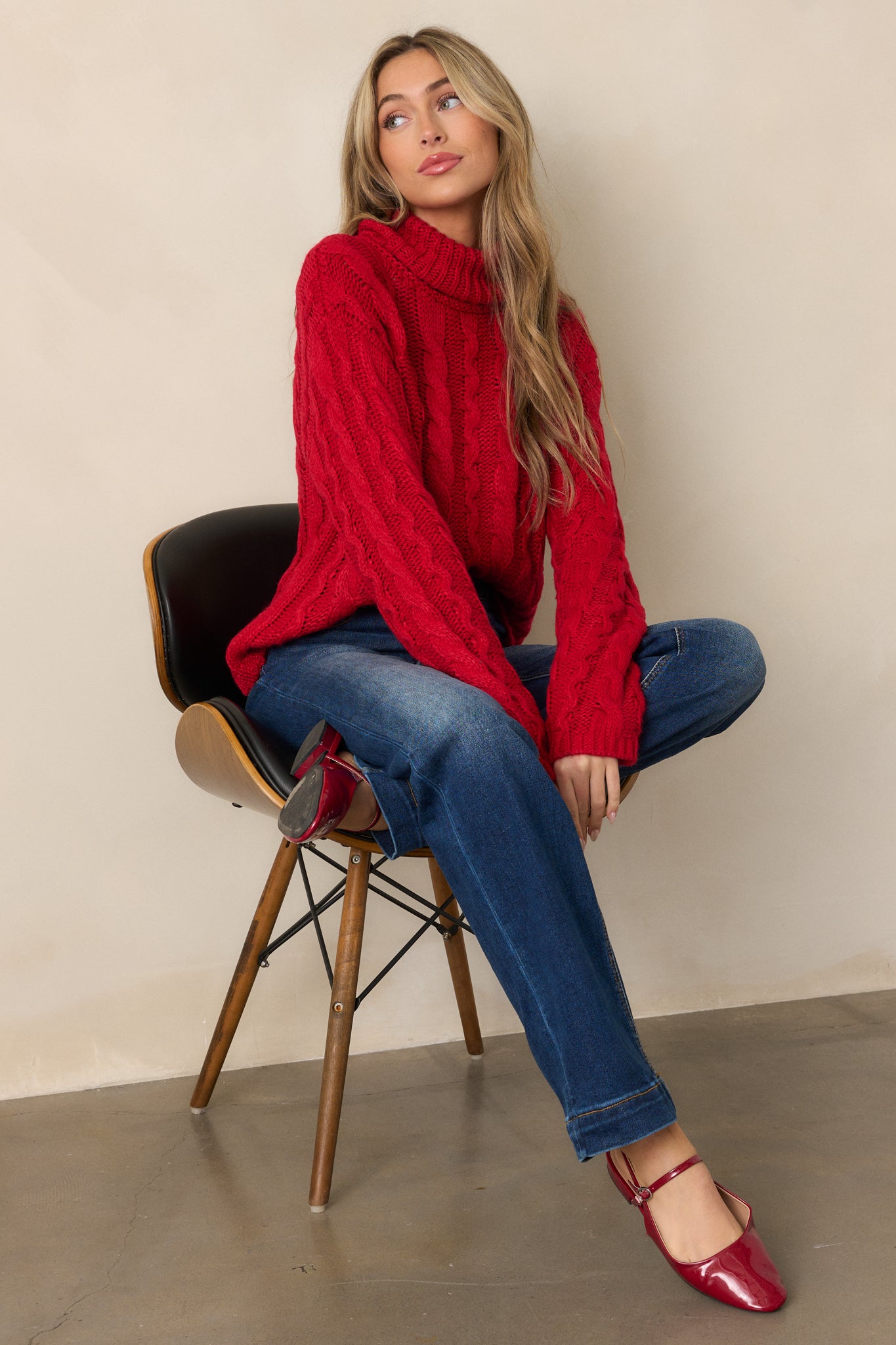 Side view of a red sweater with a turtle neck and long sleeves, highlighting the cable knit design and its loose, comfortable fit.