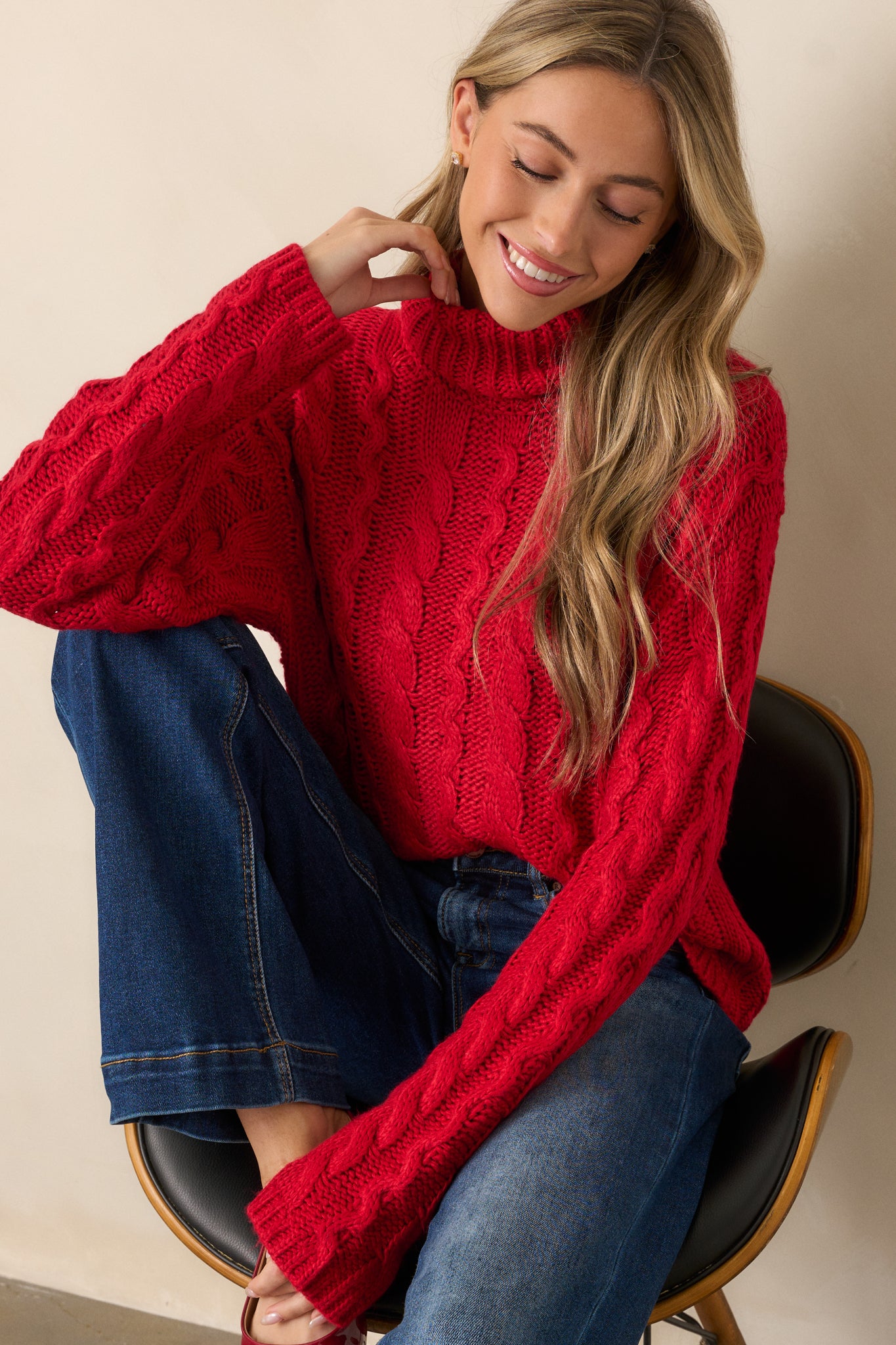 Side view of a red sweater showing its relaxed fit and long sleeves, with a detailed cable knit pattern and a cozy turtle neck.