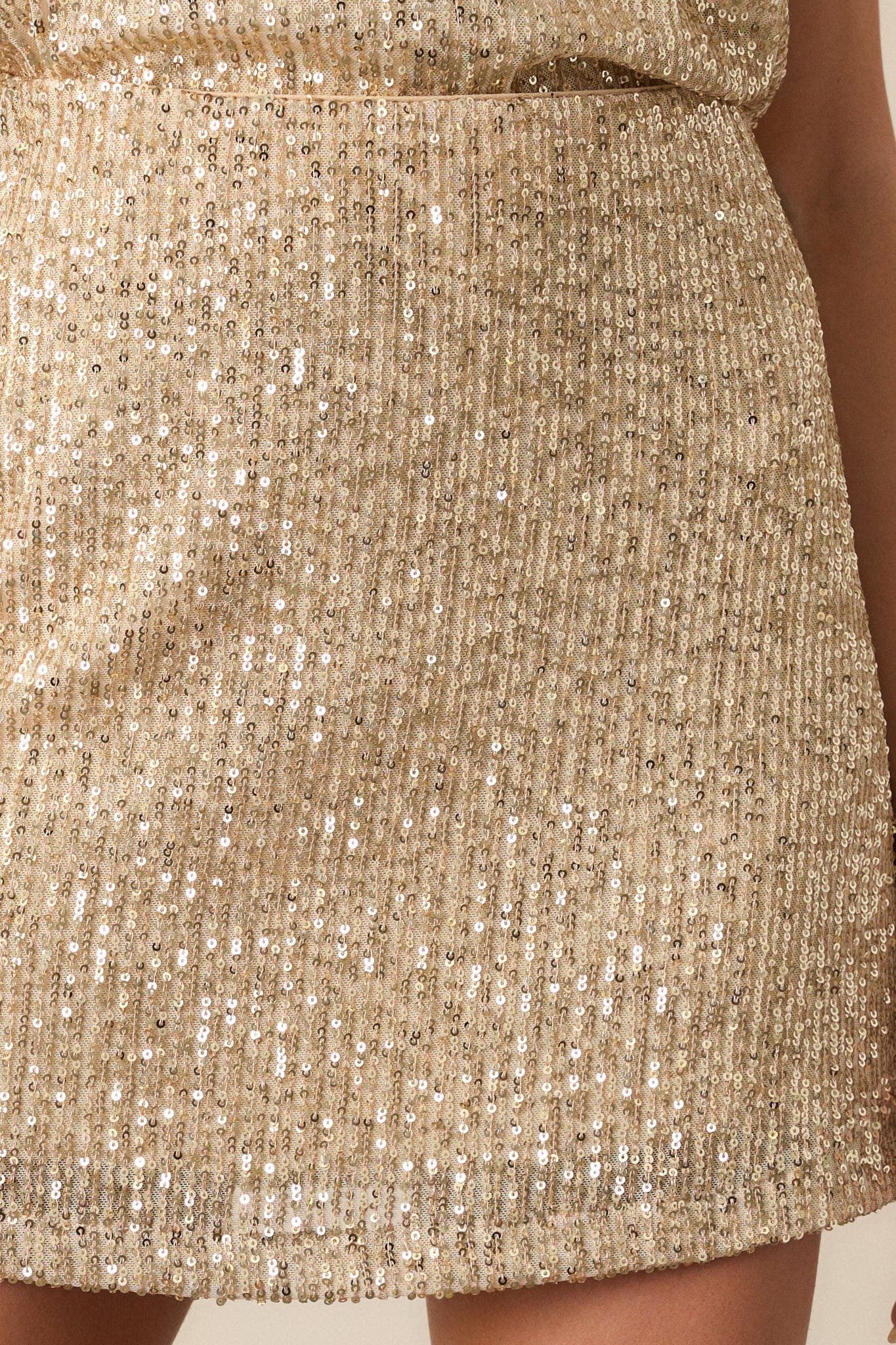 A detailed shot of the sequins on the champagne skirt, highlighting the sparkling texture of the fabric and the intricate design of the sequins arranged across the surface.