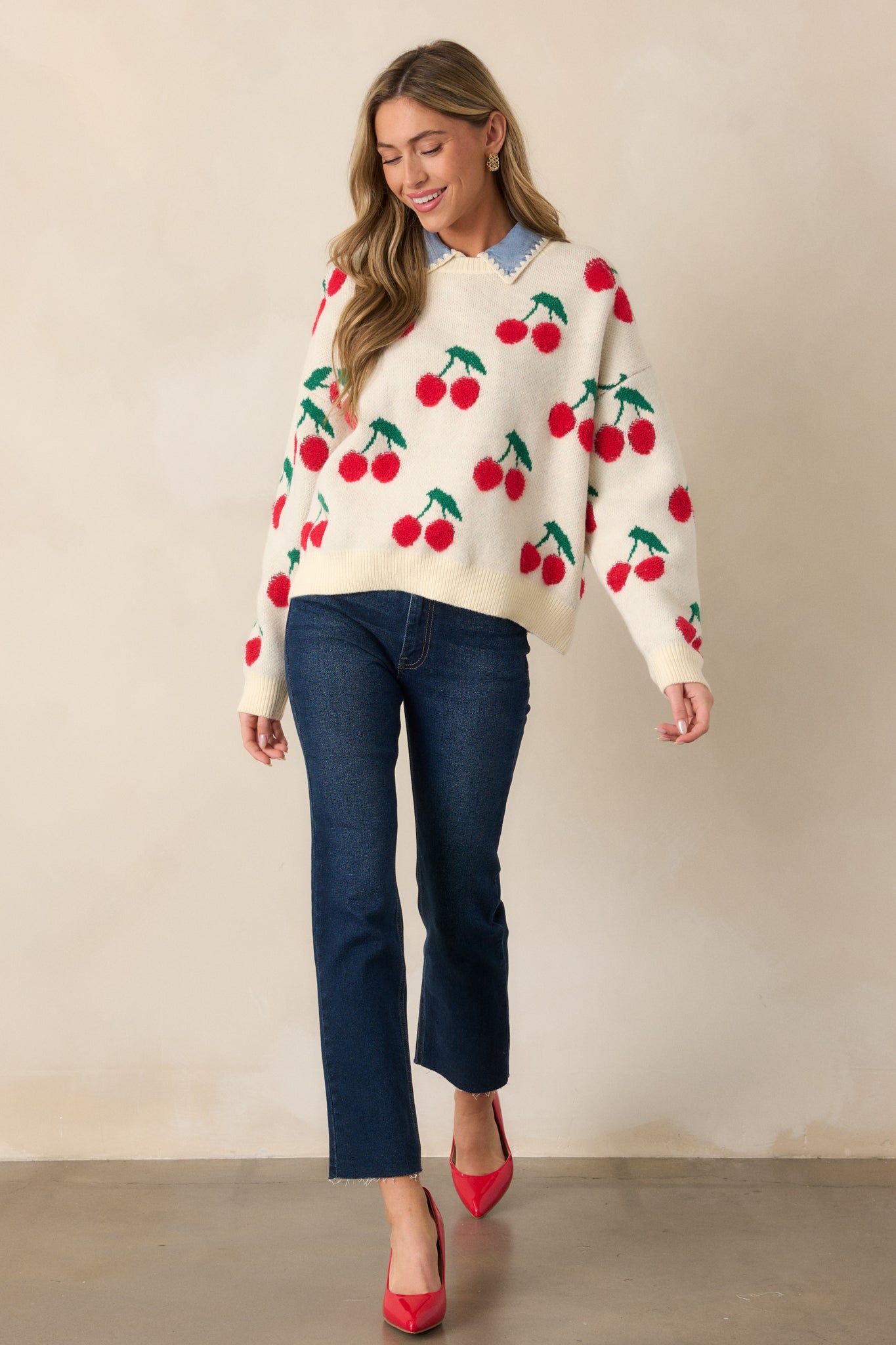 The ivory sweater is shown in full, with long sleeves and a ribbed crew neckline. The relaxed fit drapes comfortably on the body, with a playful cherry embroidered print that adds a fun touch to the sweater.