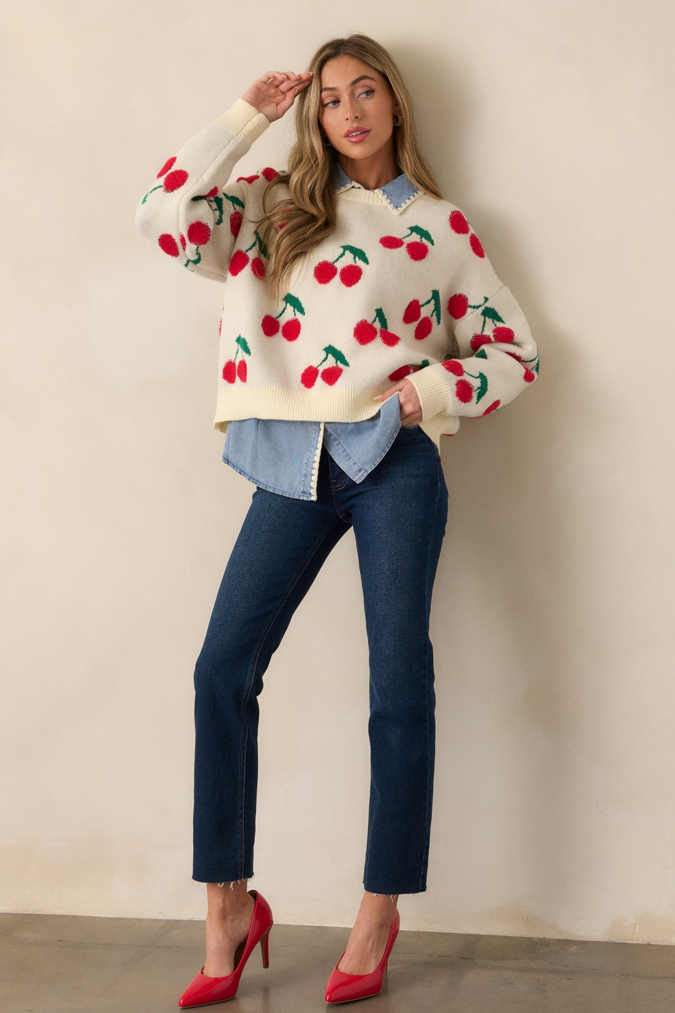 A full body shot showcasing the ivory sweater, with long sleeves and ribbed hems. The relaxed fit and fun cherry embroidery are prominent, highlighting the playful design and casual vibe of the top.