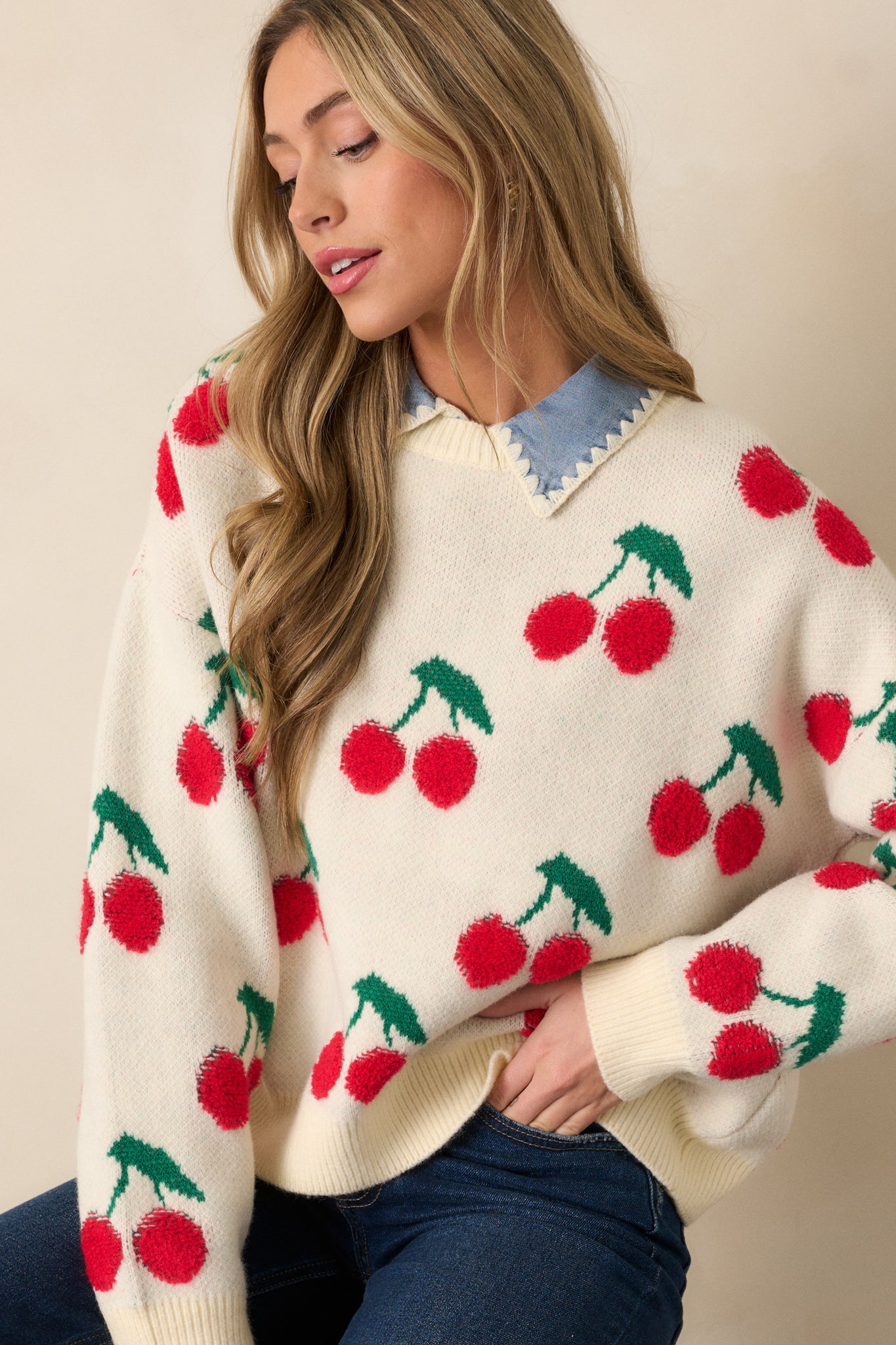 A cropped shot focusing on the ribbed cuffs of the long sleeves and the cherry embroidered details across the sweater. The relaxed fit is emphasized, giving the top a comfortable yet stylish appearance.