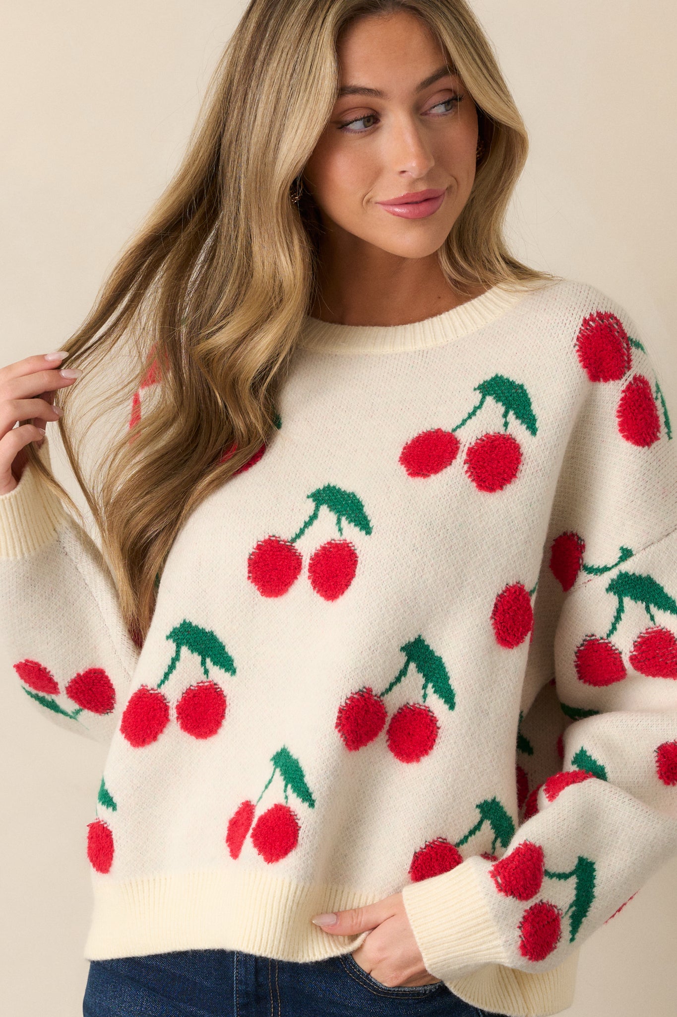 A cropped view of the ivory sweater’s ribbed crew neckline and long sleeve cuffs. The fun cherry embroidered print is clearly visible, adding a whimsical touch to the overall look.