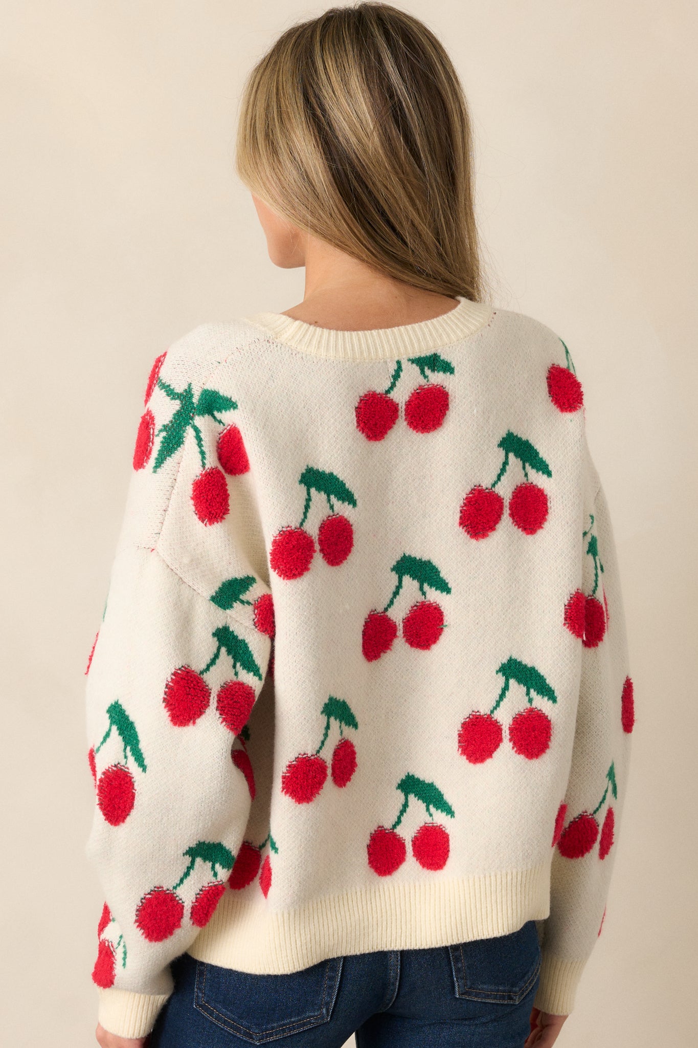 A back view of the ivory sweater, showcasing the ribbed hem and relaxed fit. The long sleeves and playful cherry embroidery are visible from behind, giving the sweater a cozy and fun look.