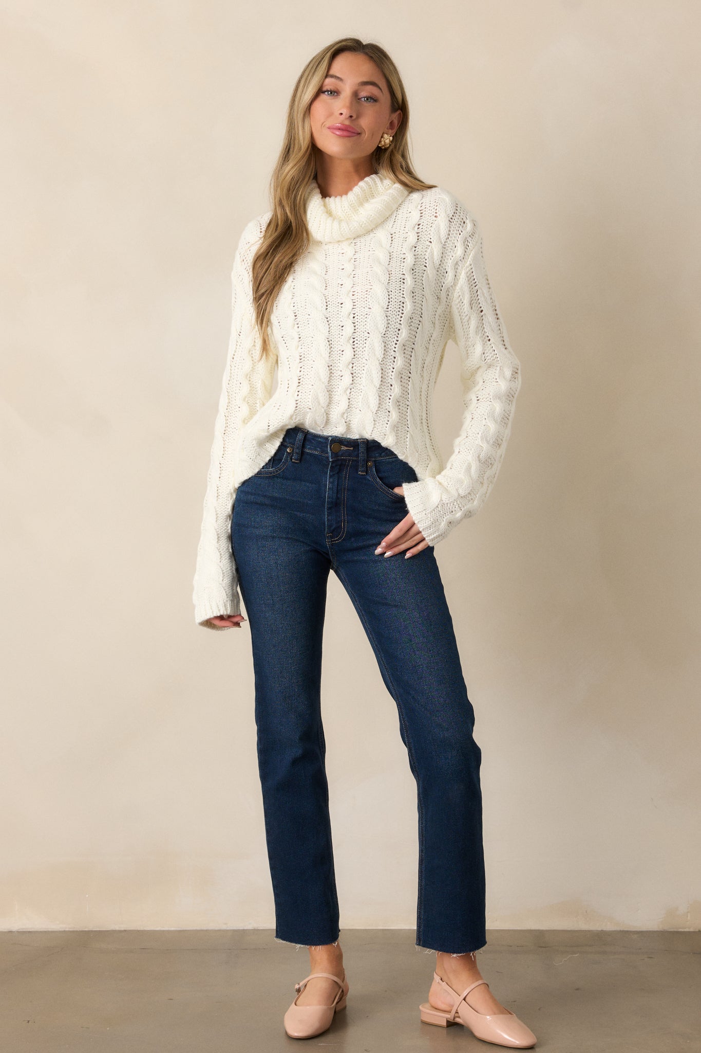 Front view of an ivory sweater with a turtle neck, featuring a beautiful cable knit design, long sleeves, and a relaxed fit.