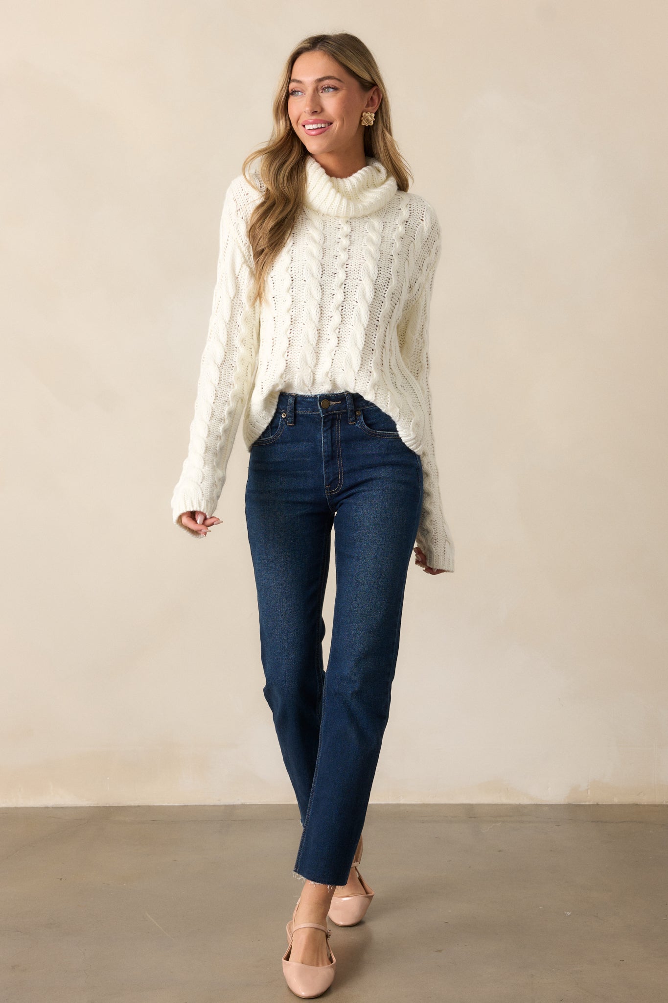 Side view of an ivory sweater with a turtle neck and long sleeves, highlighting the cable knit design and its loose, comfortable fit.