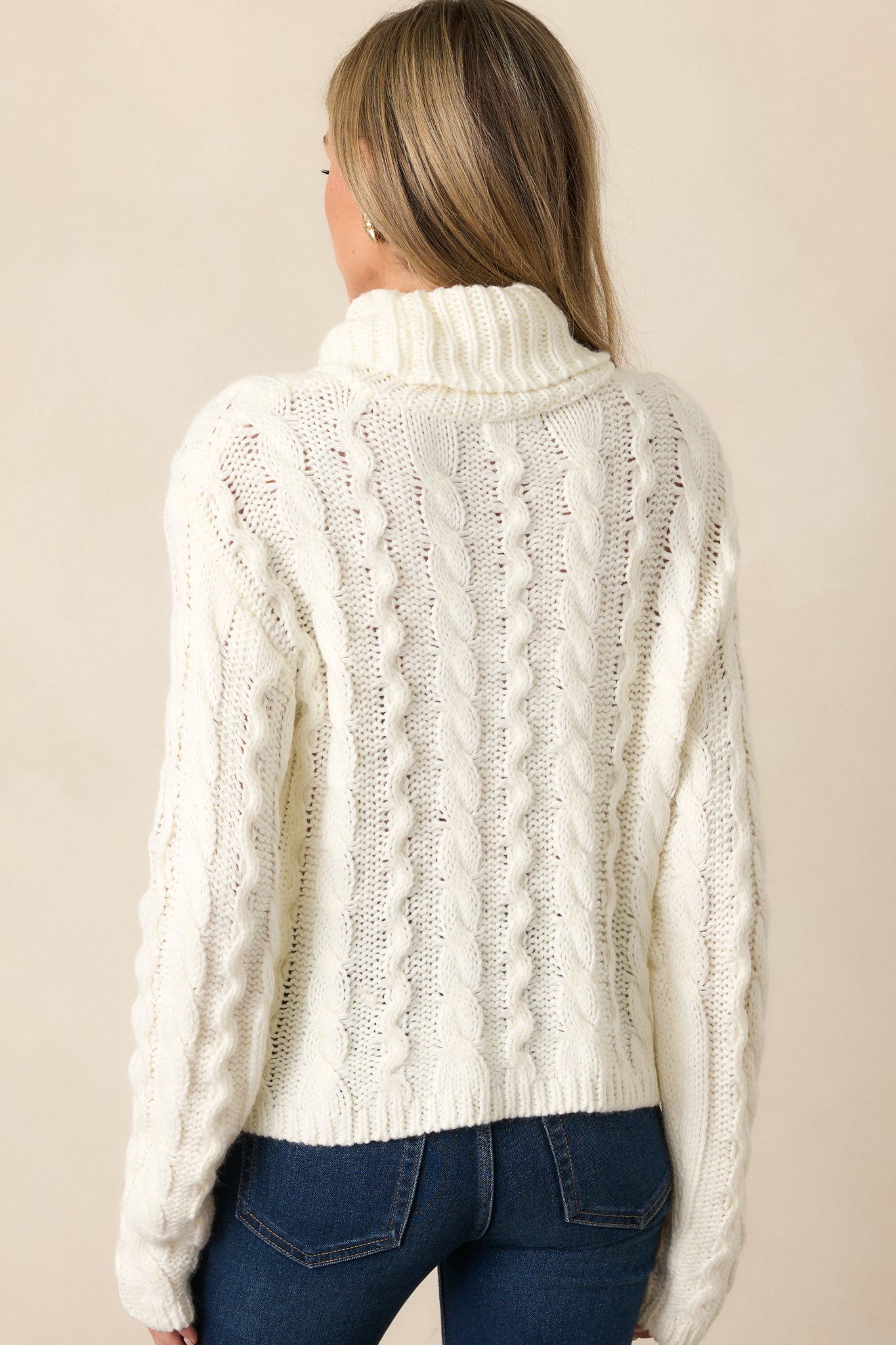 Back view of the ivory sweater, emphasizing the relaxed fit, long sleeves, and the intricate cable knit design running down the back.