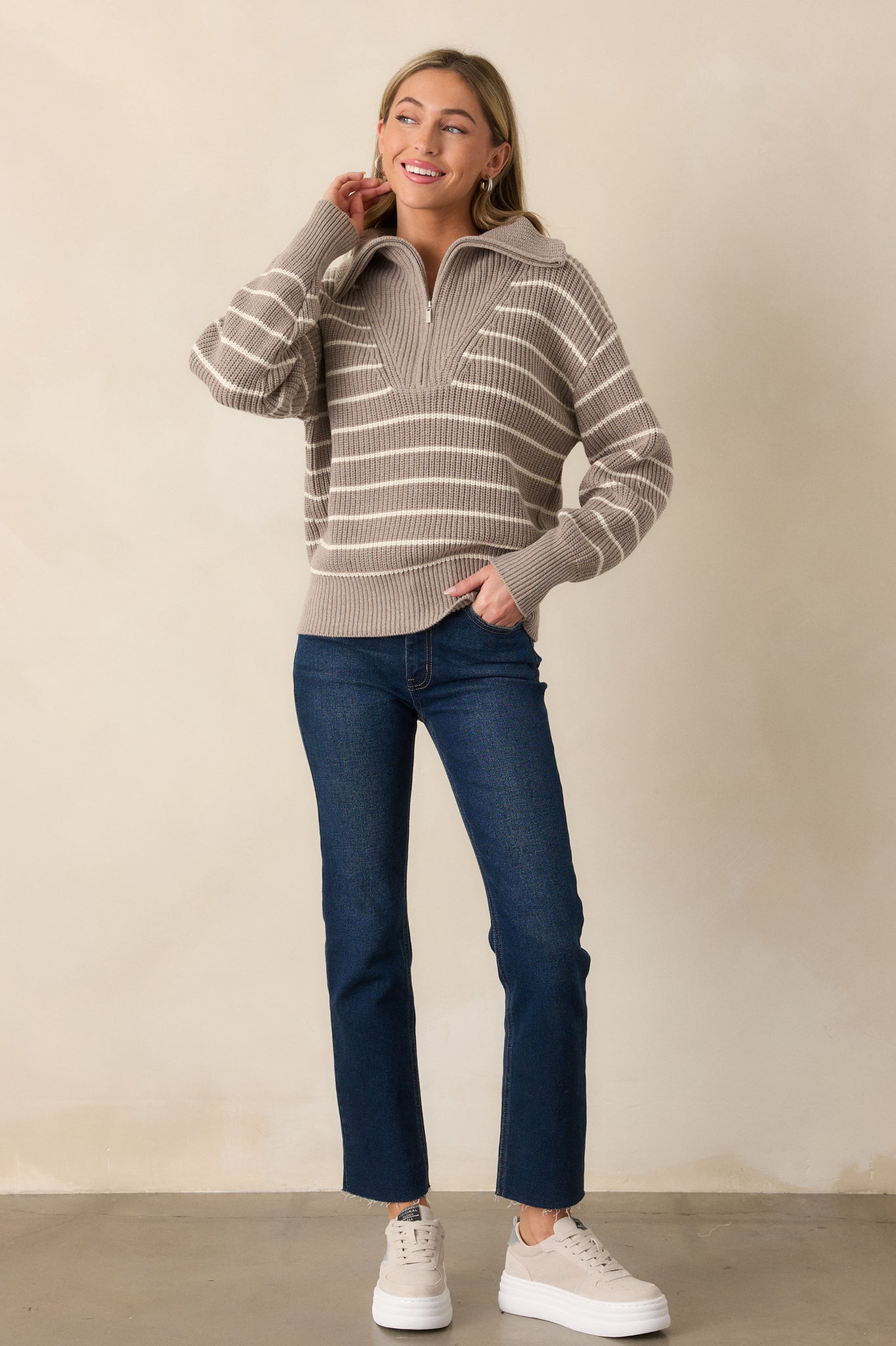 A full-body view of a heather taupe sweater featuring an oversized collar neckline and a functional half zip front. The sweater has an ivory stripe pattern across the body, rib knit hems, and long sleeves, creating a cozy, stylish look.