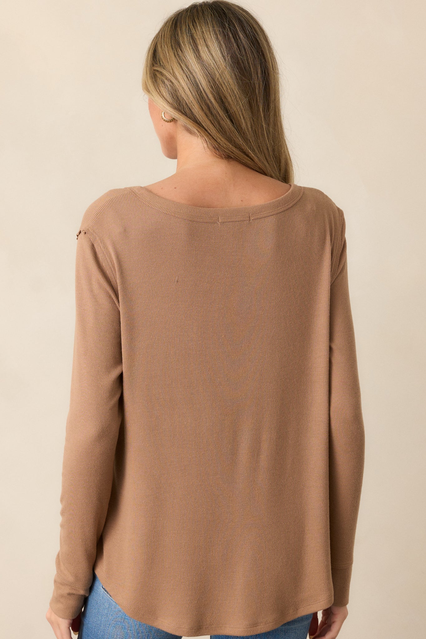 Back view of the tan top, highlighting the soft ribbed texture, long sleeves, and curved bottom hem that create a flattering fit.