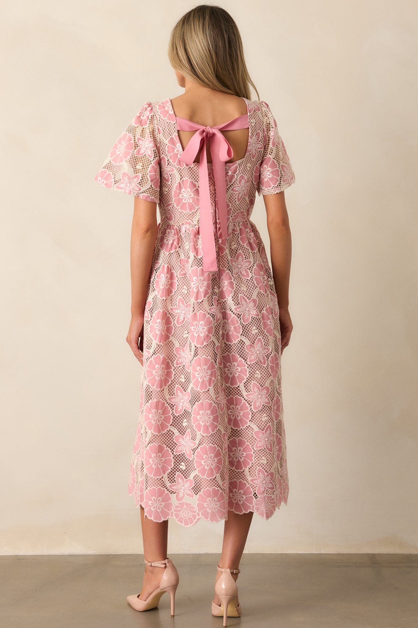 A back view of the pink dress, showing the discrete zipper closure and the seamless transition from the embroidered floral design to the sheer embroidered sleeves.