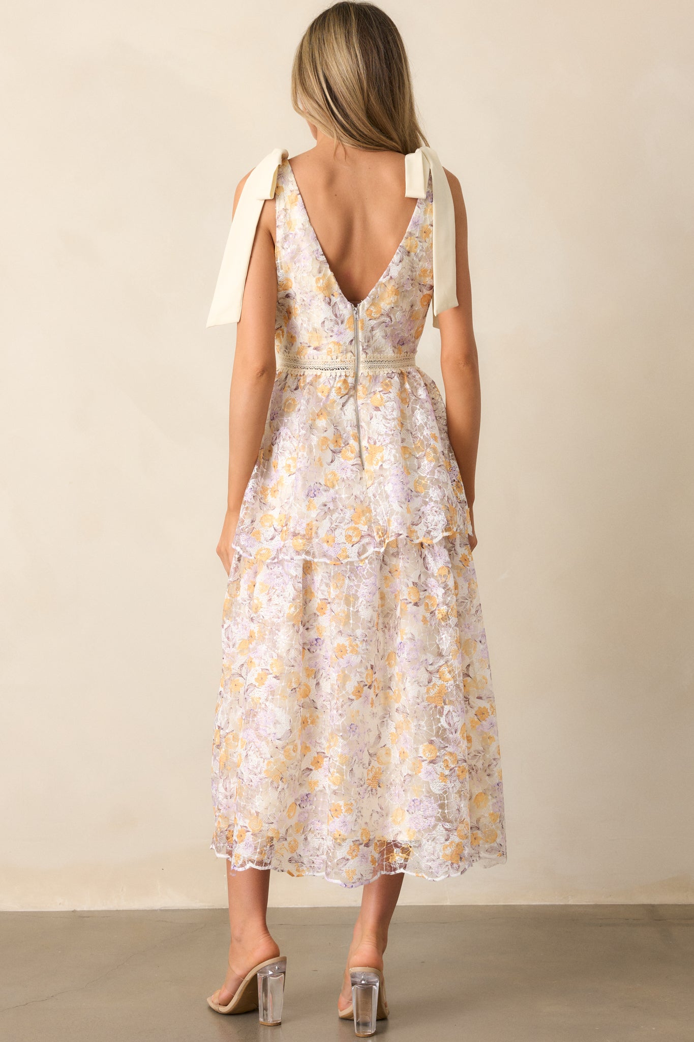 A back view of the apricot midi dress showing the zipper closure, ribbon ties, and the continuation of the floral embroidered pattern.