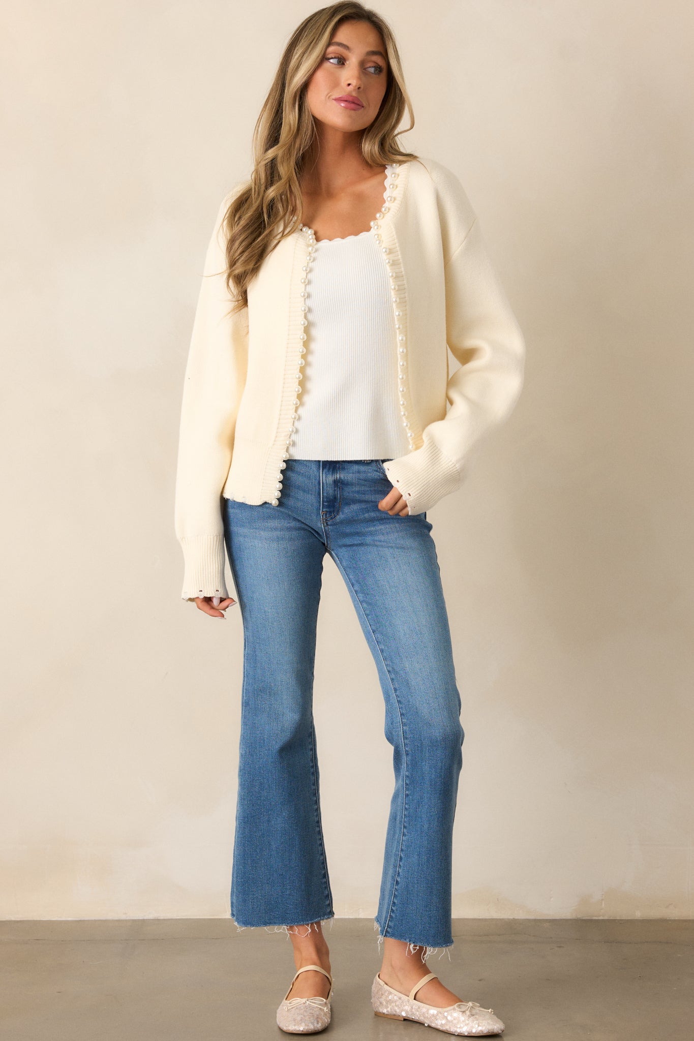 This ivory cardigan showcases its rounded neckline and elegant faux pearl trim, paired with a relaxed no-button closure.