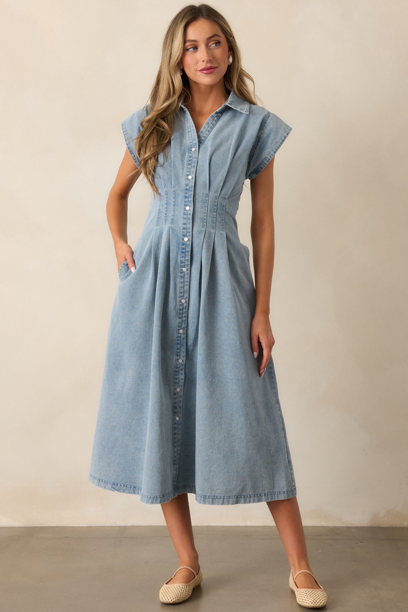 Light wash dress showcasing a pleated waist, cap sleeves, and functional pockets, with a full view of the button-down front design.