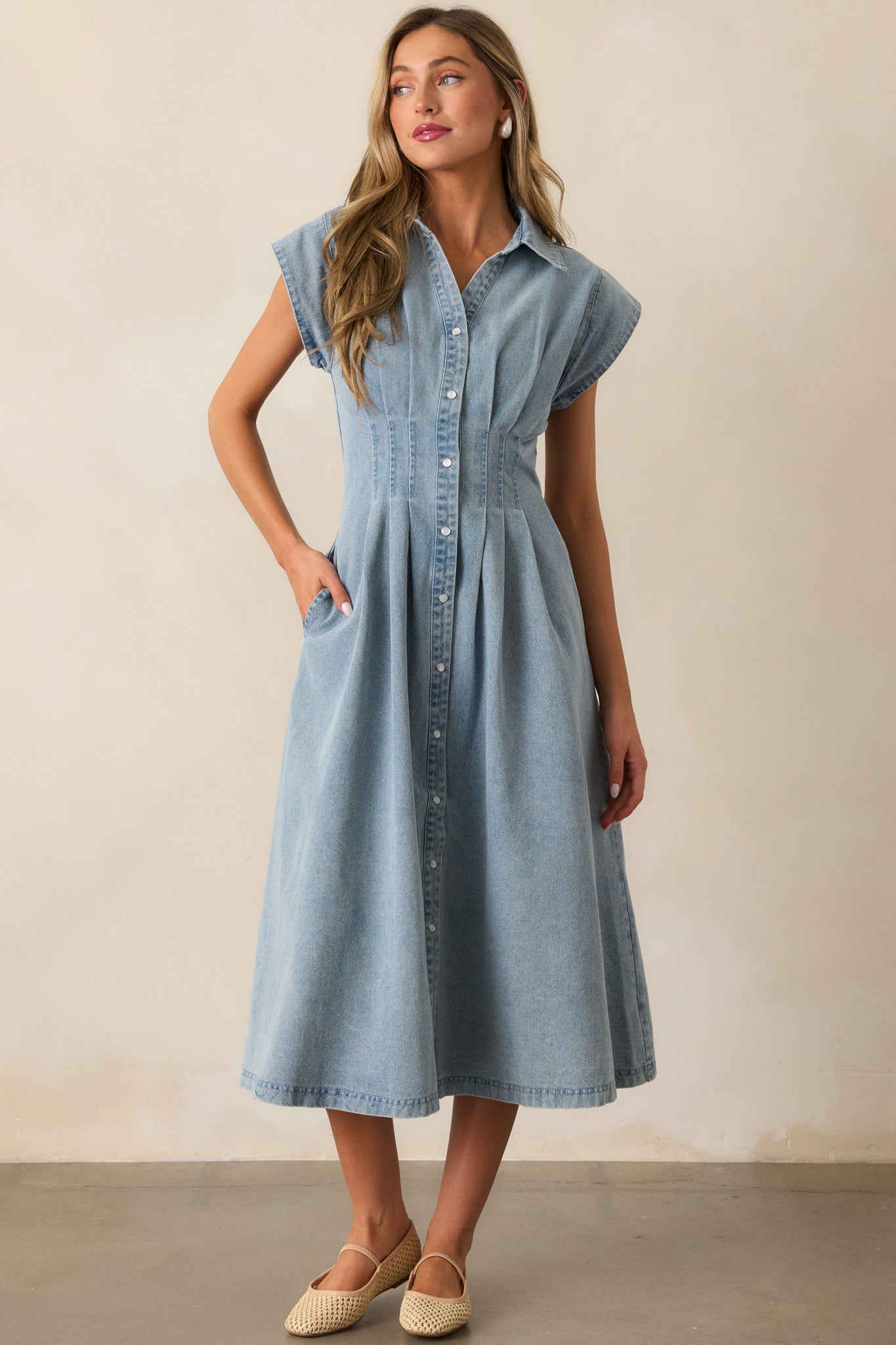 Light wash dress with a button-front design, functional side pockets, cap sleeves, and a pleated waist, captured in full view.