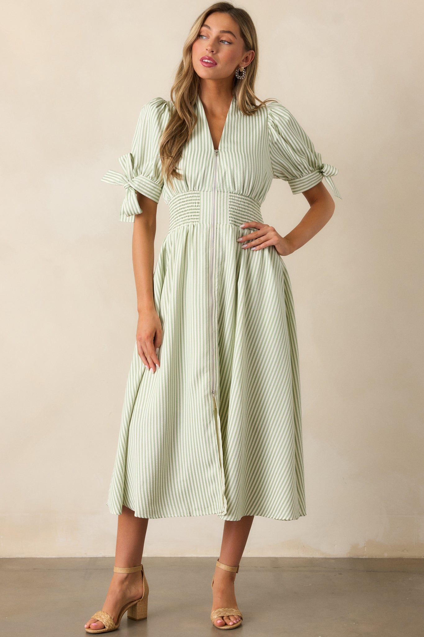 Green stripe dress with a smocked waist, functional pockets, a V-neck neckline, and tie details on the long sleeves, styled with a front zipper.