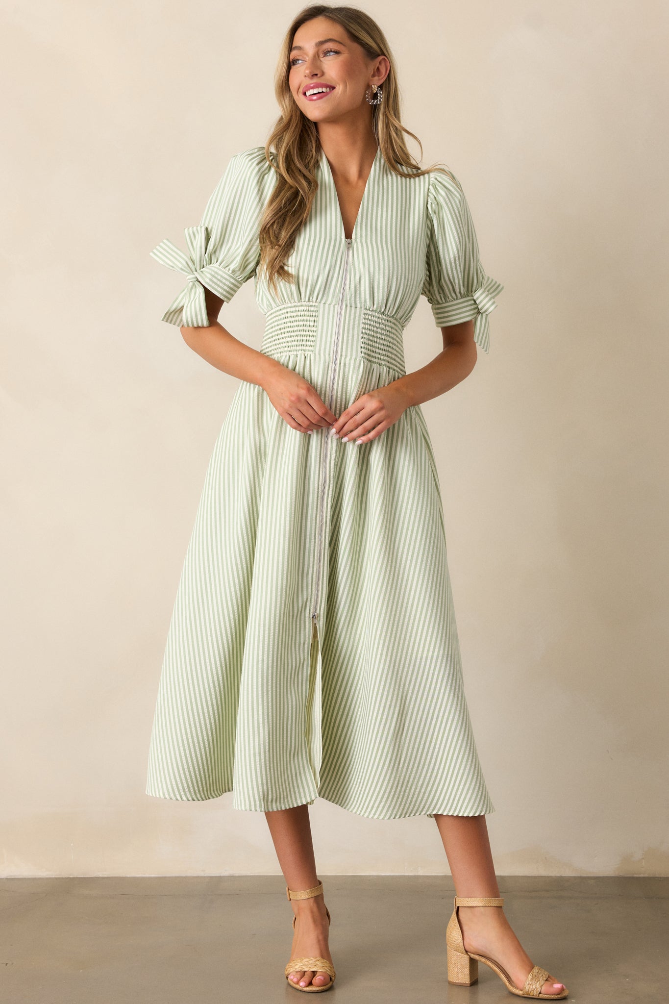 Green stripe dress featuring a fitted waist with smocking detail, a V-neck neckline leading to a front zipper, and tie accents at the bottom of the sleeves.