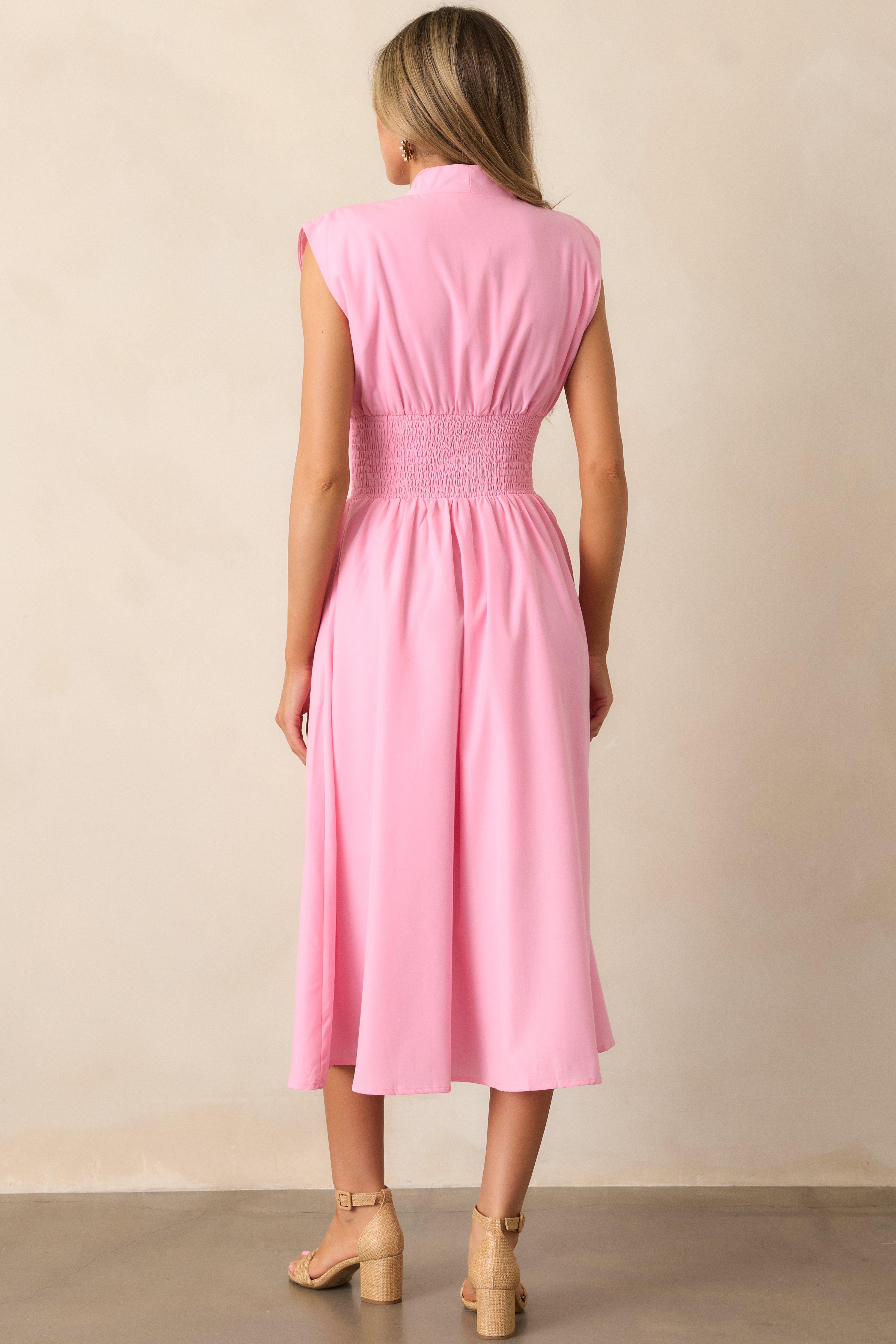 Back view of a baby pink midi dress highlighting the overall fit, padded shoulders, and fully smocked waist.