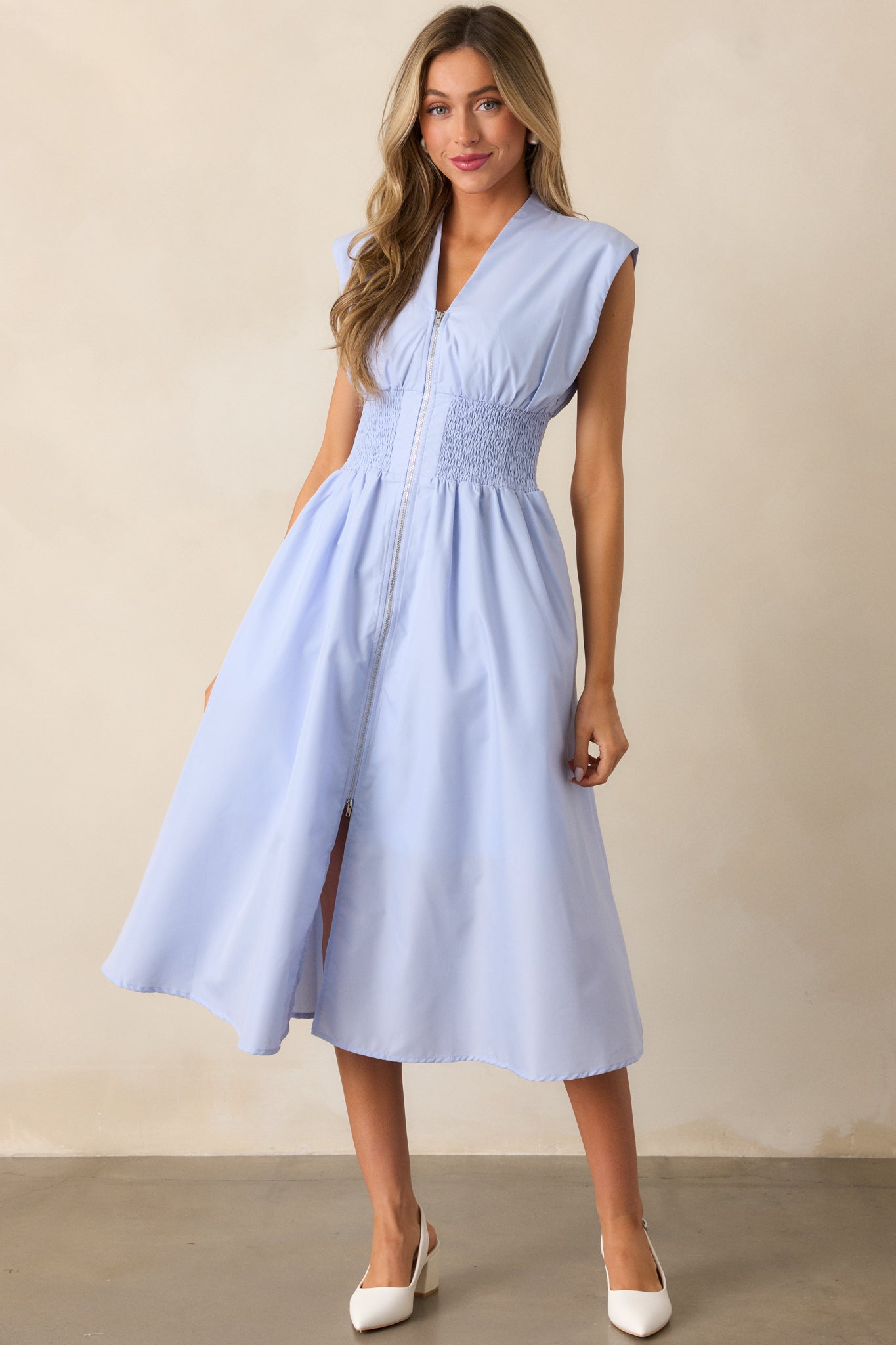 A baby blue midi dress with a v-neckline, capped sleeves, and a front slit, designed with a smocked waist and functional hip pockets for a stylish, practical look.