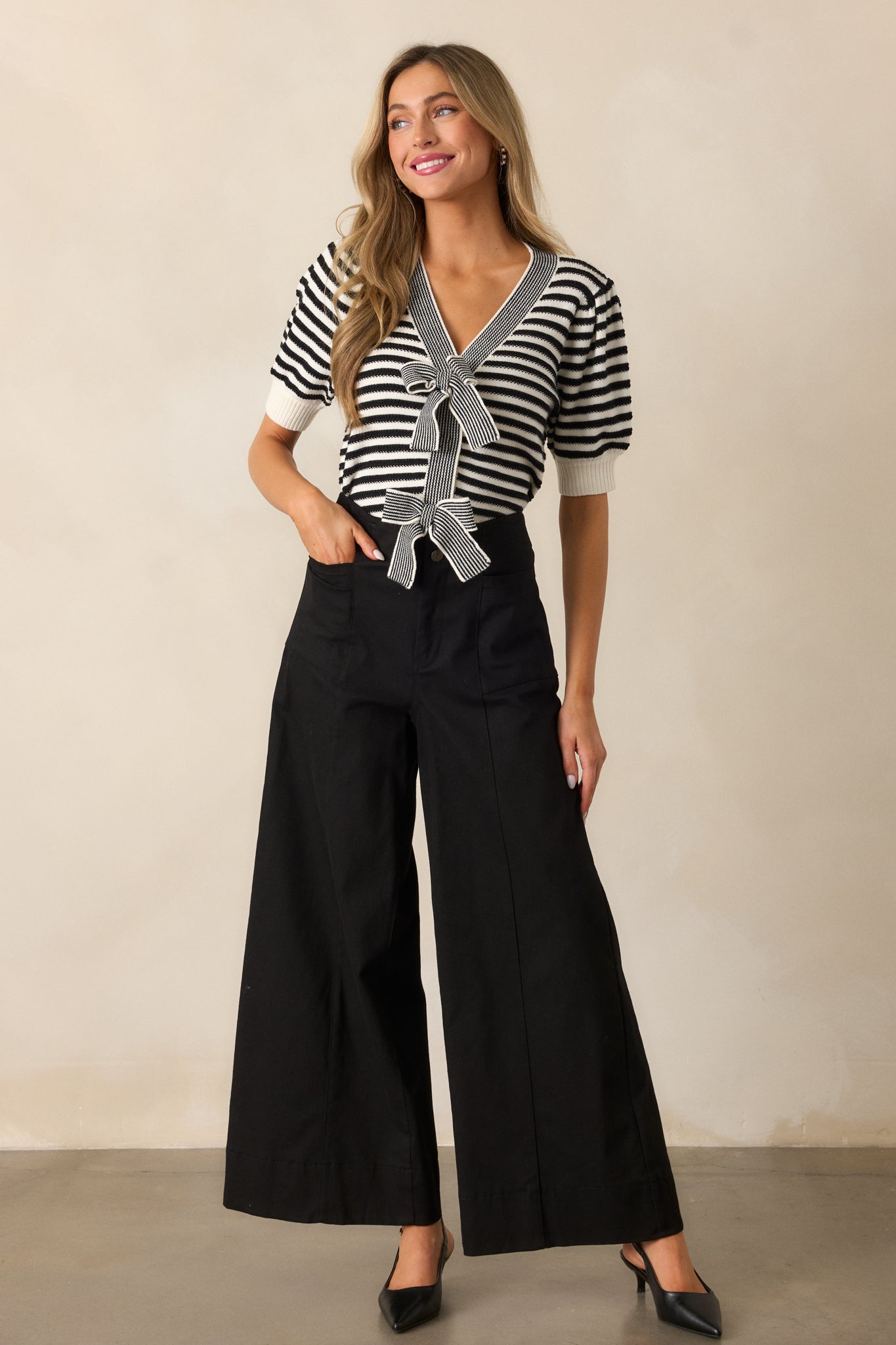 A black top styled with a v-neckline, a striped black and white pattern, and puff sleeves with ribbed cuffs, displayed in a complete outfit.