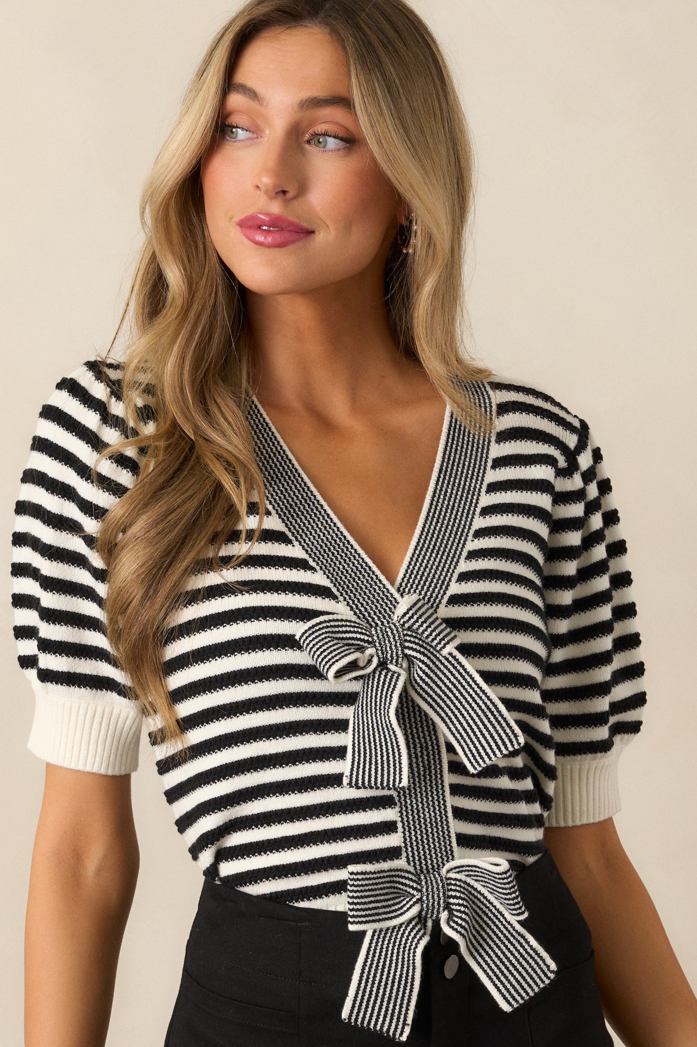 Detailed view of the black and white striped top, focusing on the v-neckline, bow front detail, and puff sleeve cuffs.