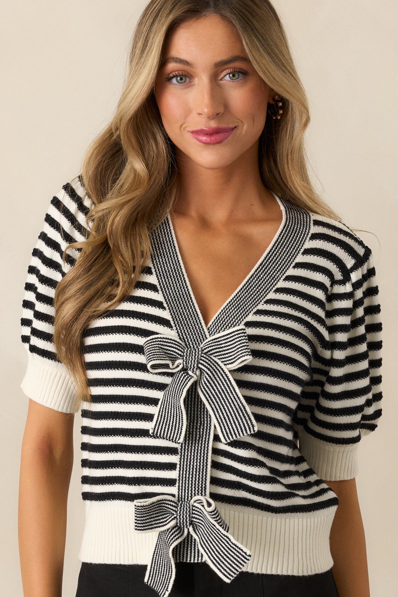 A black top highlighting the v-neckline, striped pattern, and bow front detail, with puff sleeves and ribbed cuffs in view.