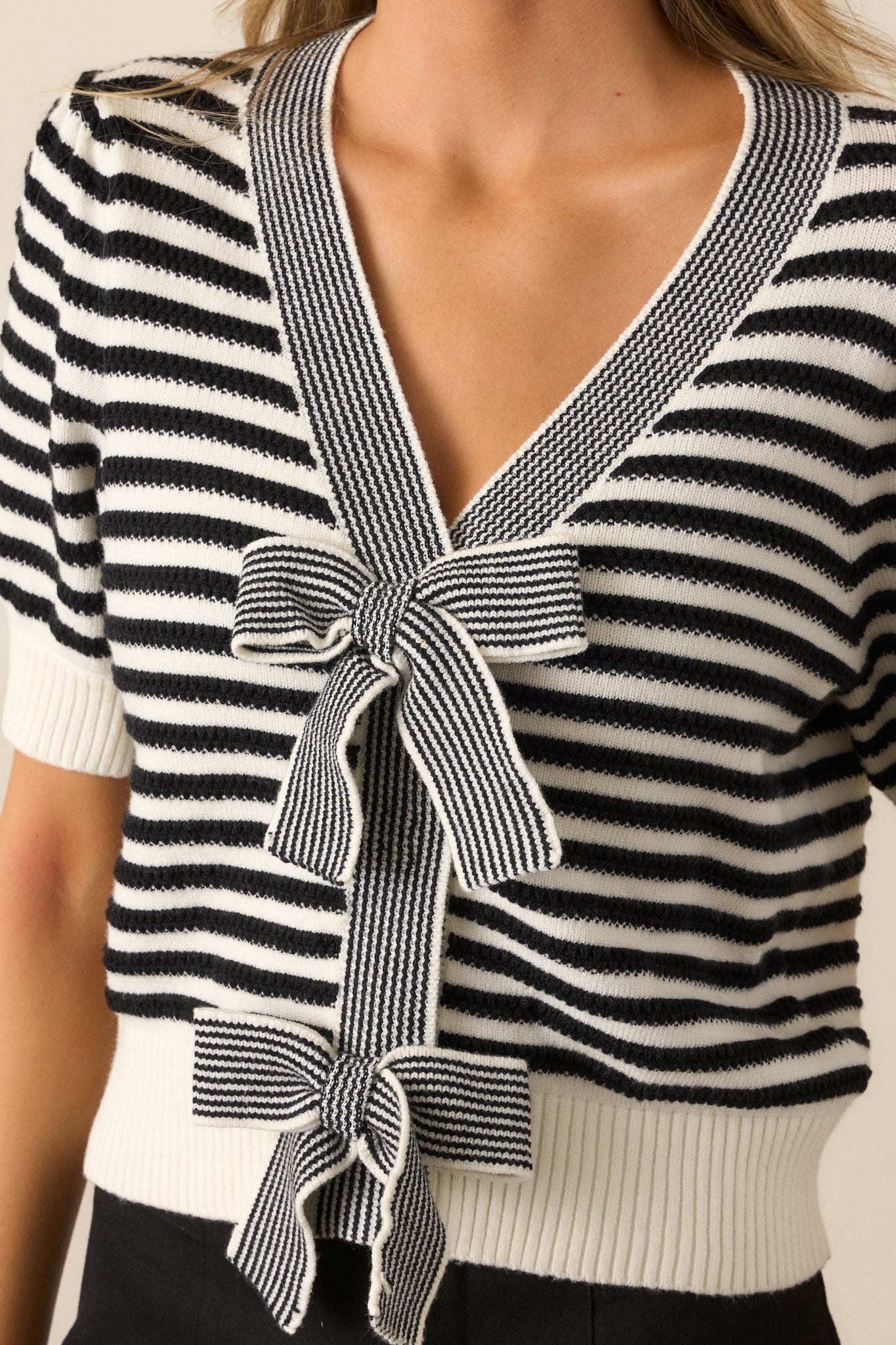 Close-up of the black top’s striped print, bow front feature, and ribbed puff sleeve cuff design.